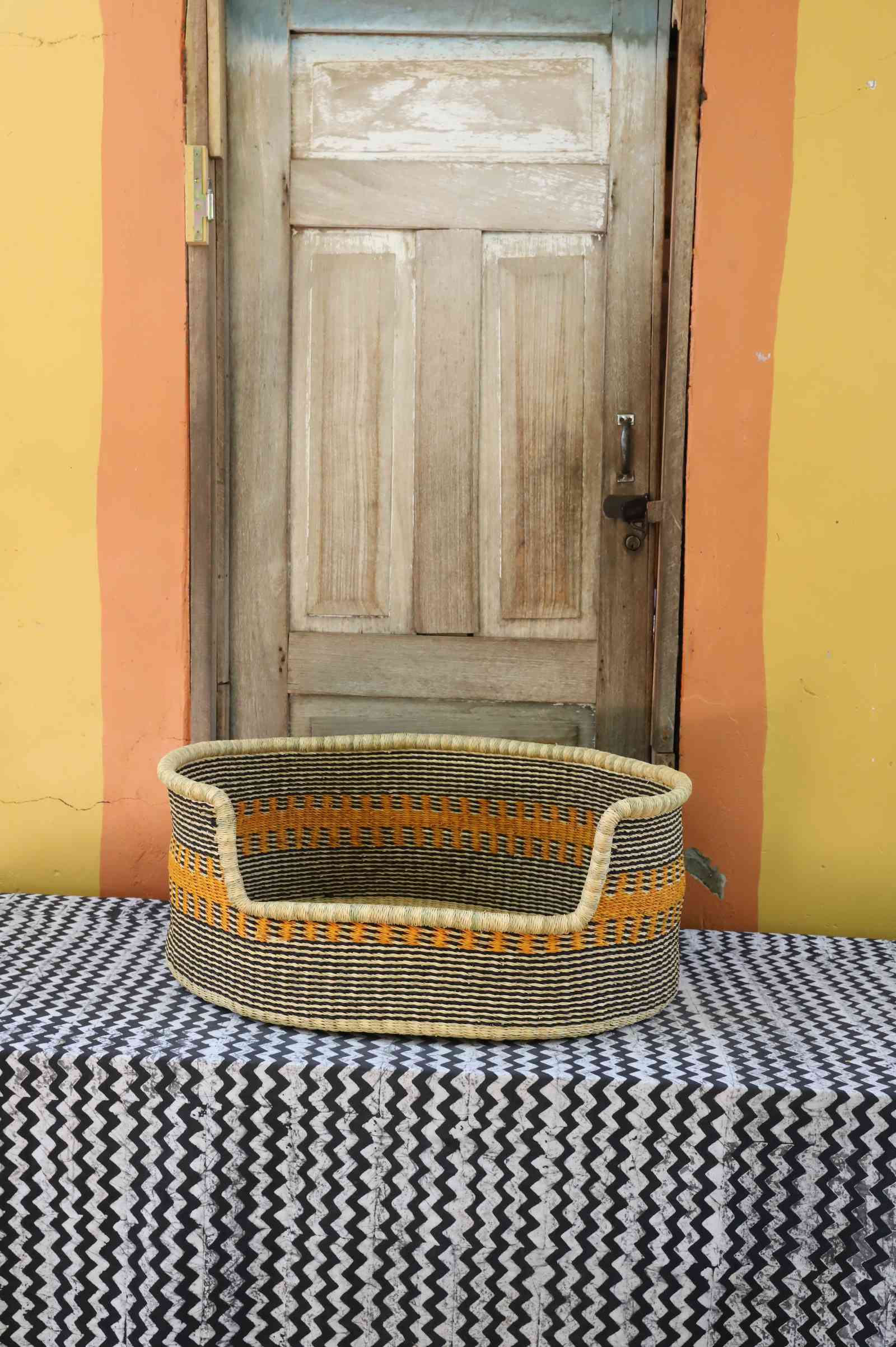 Large handwoven Bolga pet bed in natural straw with a wide orange and yellow banded central stripe.