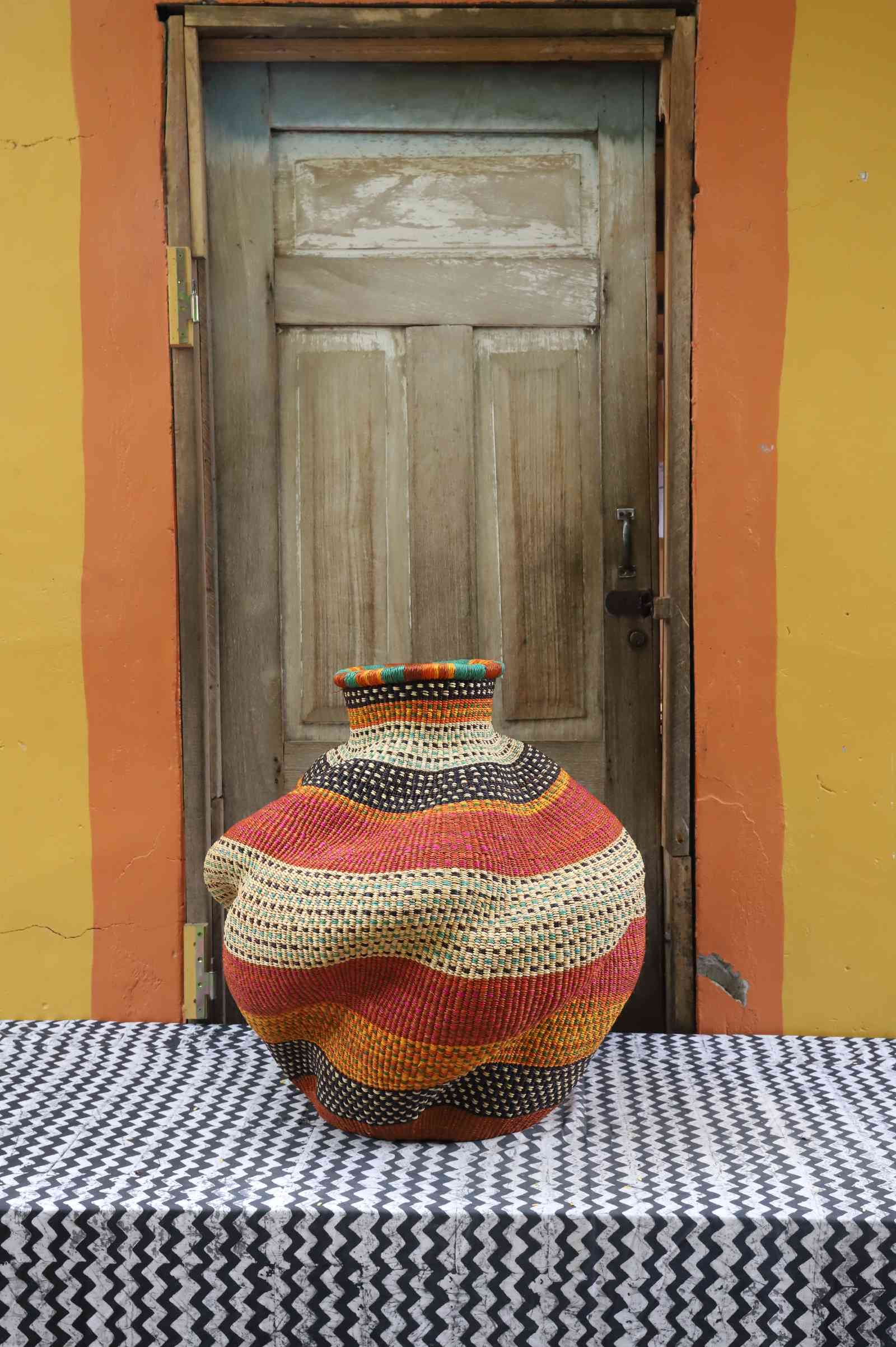 Medium handwoven Bolga art basket in rust-orange with dotted bands, side view of the sculpted urn.