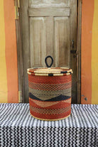 Handwoven Bolga laundry basket with coiled rim and lid in rust-orange with a dark wave motif and natural rim.
