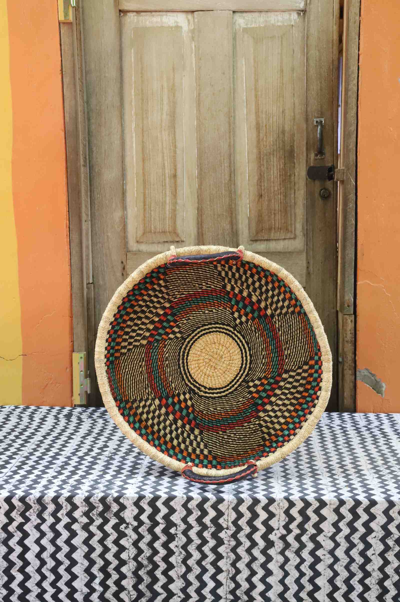 Handwoven Bolga wall tray disc in natural straw with fine dark concentric bands and radial dark rays.