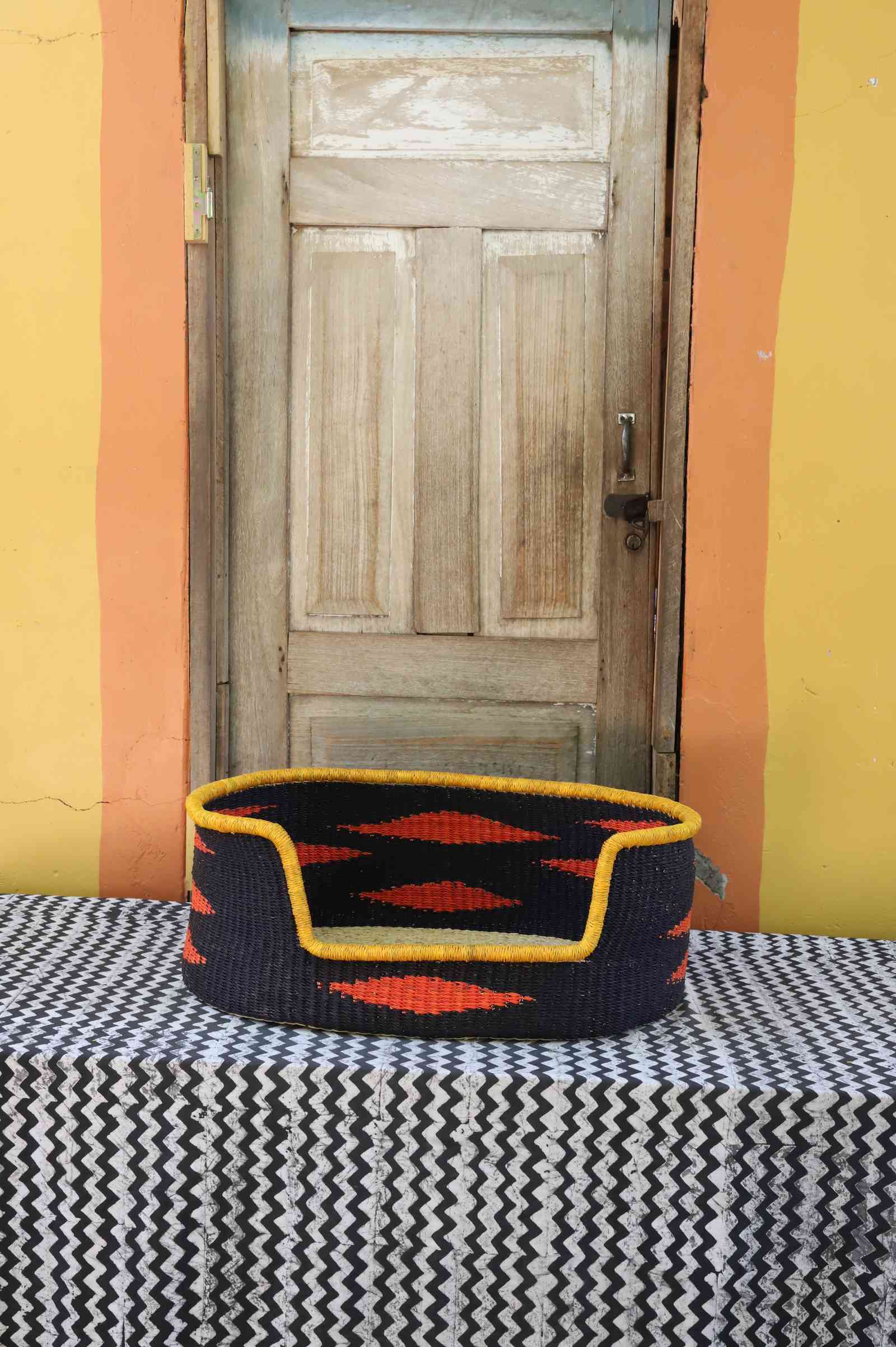 Medium handwoven Bolga pet bed in bold black with orange diamond flames and a yellow banded rim.