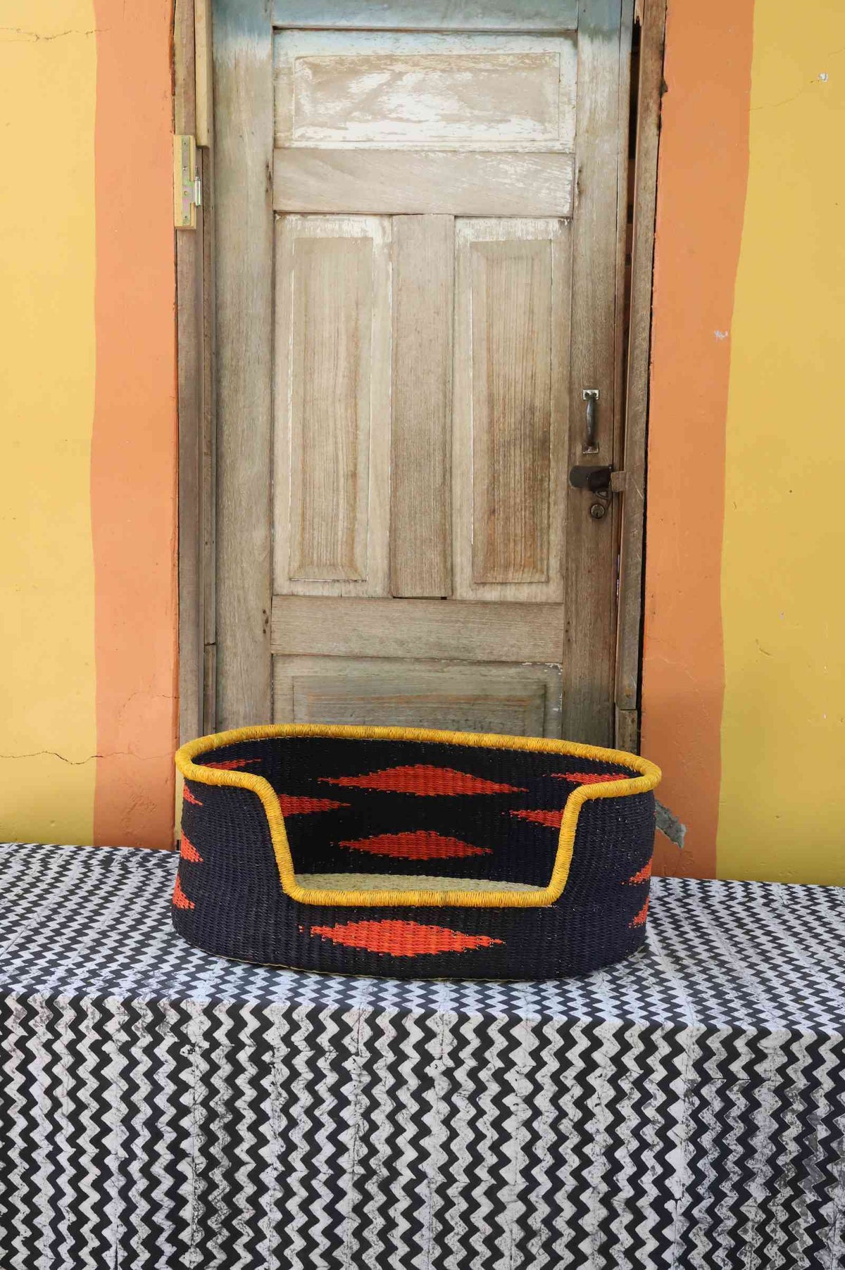 Medium handwoven Bolga pet bed in bold black with orange diamond flames and a yellow banded rim.