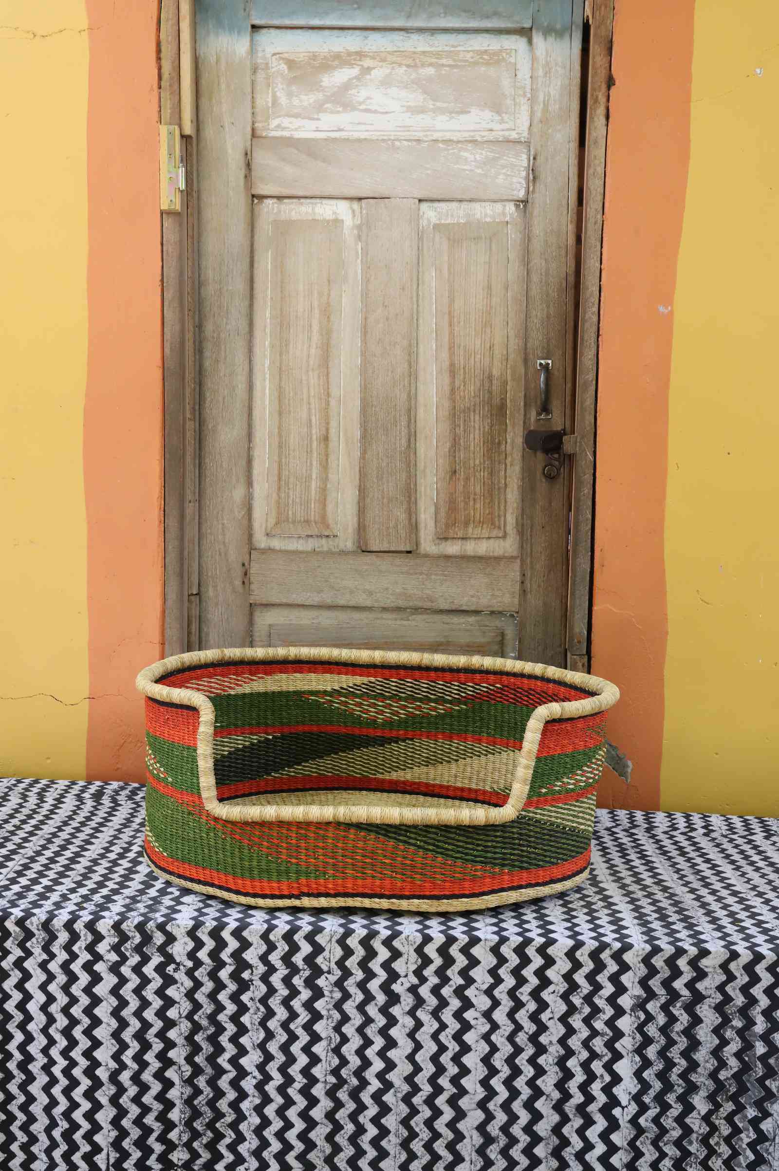Large handwoven Bolga pet bed in natural straw with green, red and orange horizontal banded stripes.