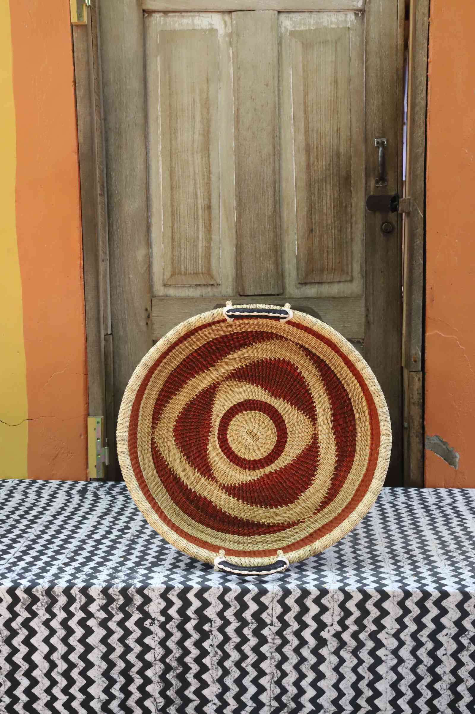 Handwoven Bolga wall tray disc in natural straw with concentric rust-red bullseye rings.