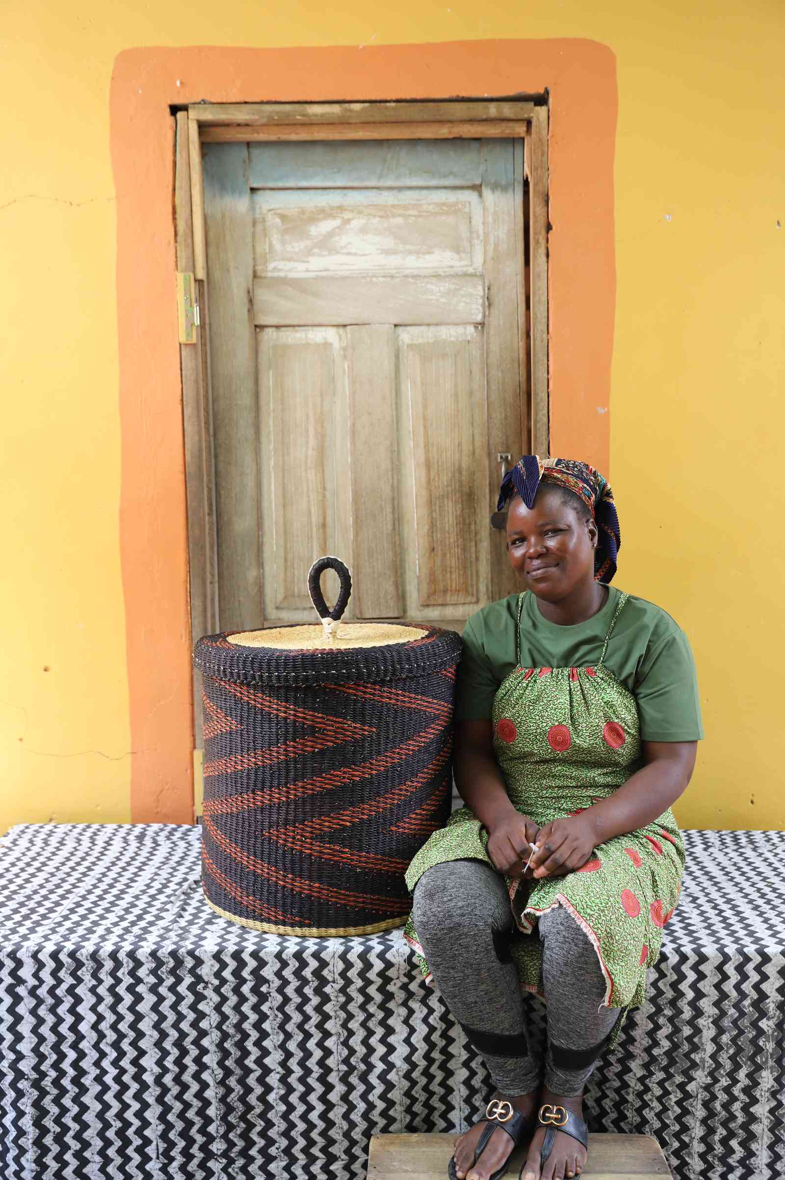Handwoven Bolga laundry basket in dark blue with rust-orange zigzag, beside a seated woman in green.