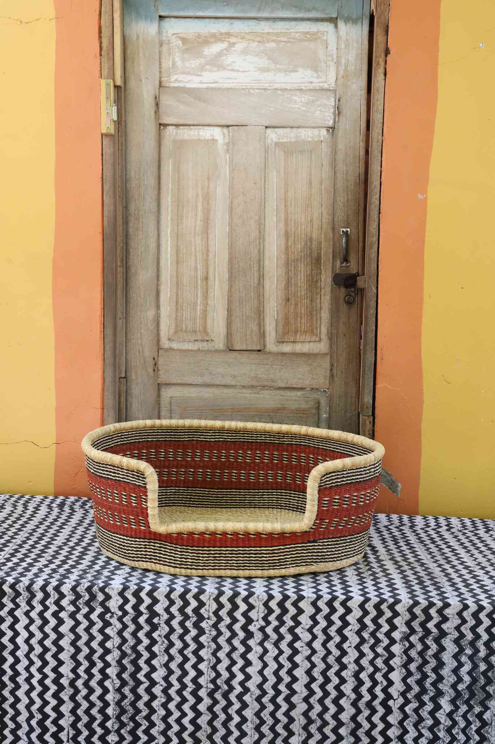 Medium handwoven Bolga pet bed in natural straw with red horizontal banded stripes.