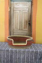 Medium handwoven Bolga pet bed in natural straw with red horizontal banded stripes.