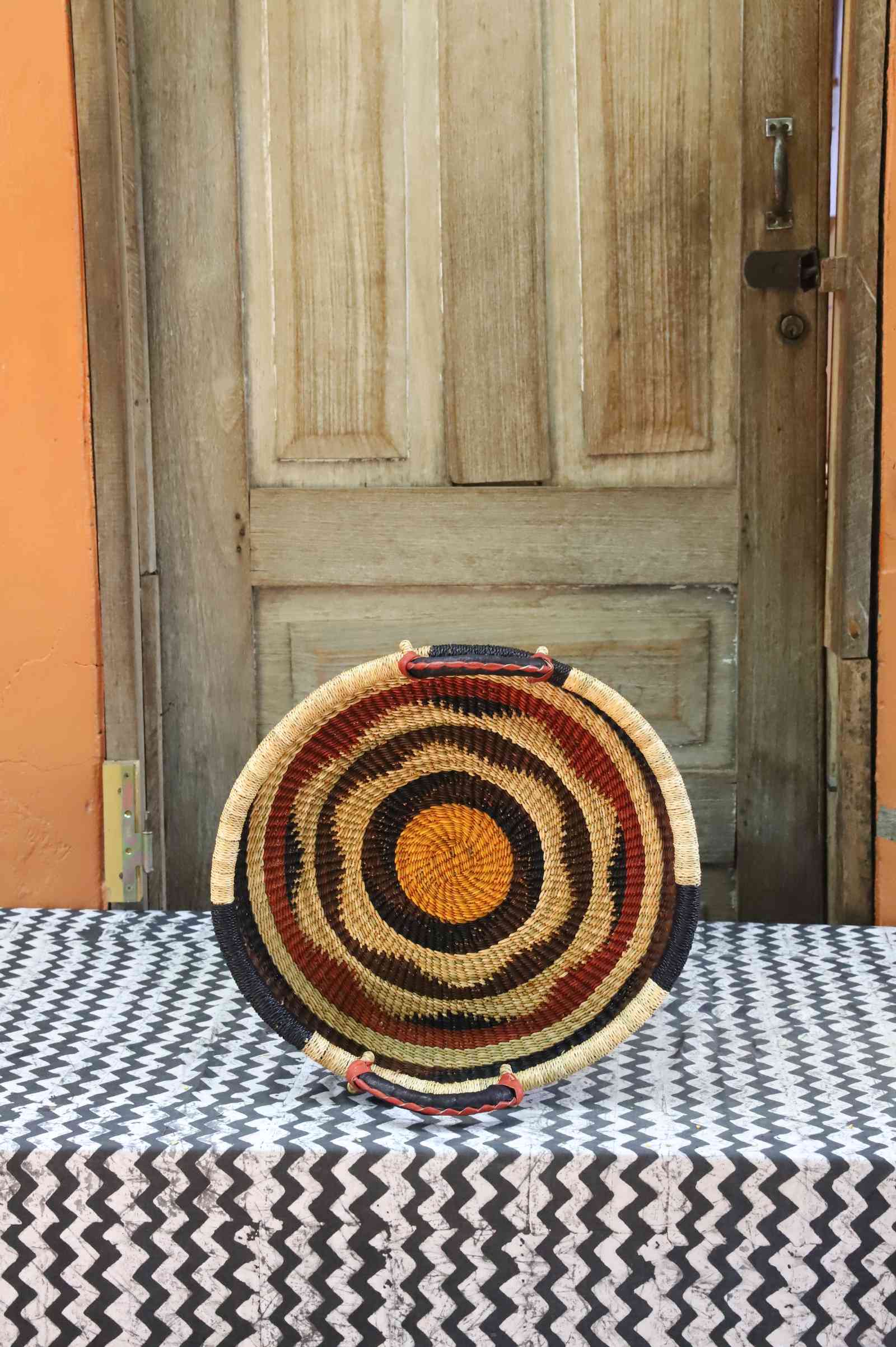 Handwoven Bolga wall tray disc in concentric red, black, yellow and natural bands with an orange centre.