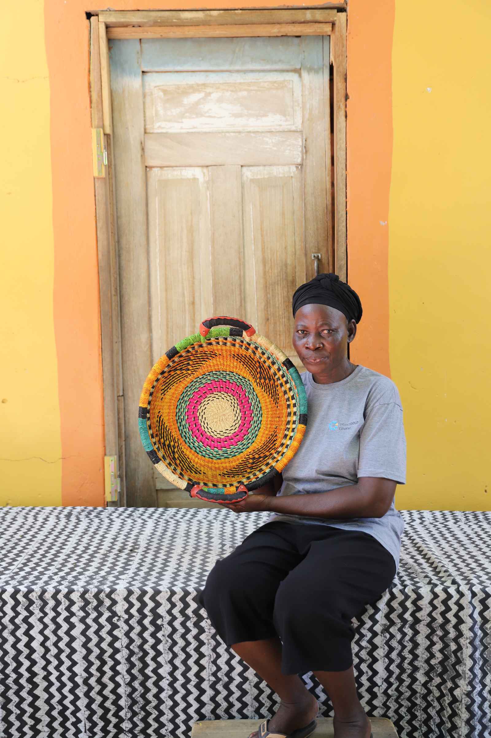 Handwoven Bolga wall tray disc with fine multicolour bands, held by a seated woman in grey.