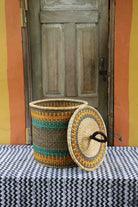 Handwoven Bolga laundry basket with lid removed, natural body with yellow-orange and teal stripes and lid.