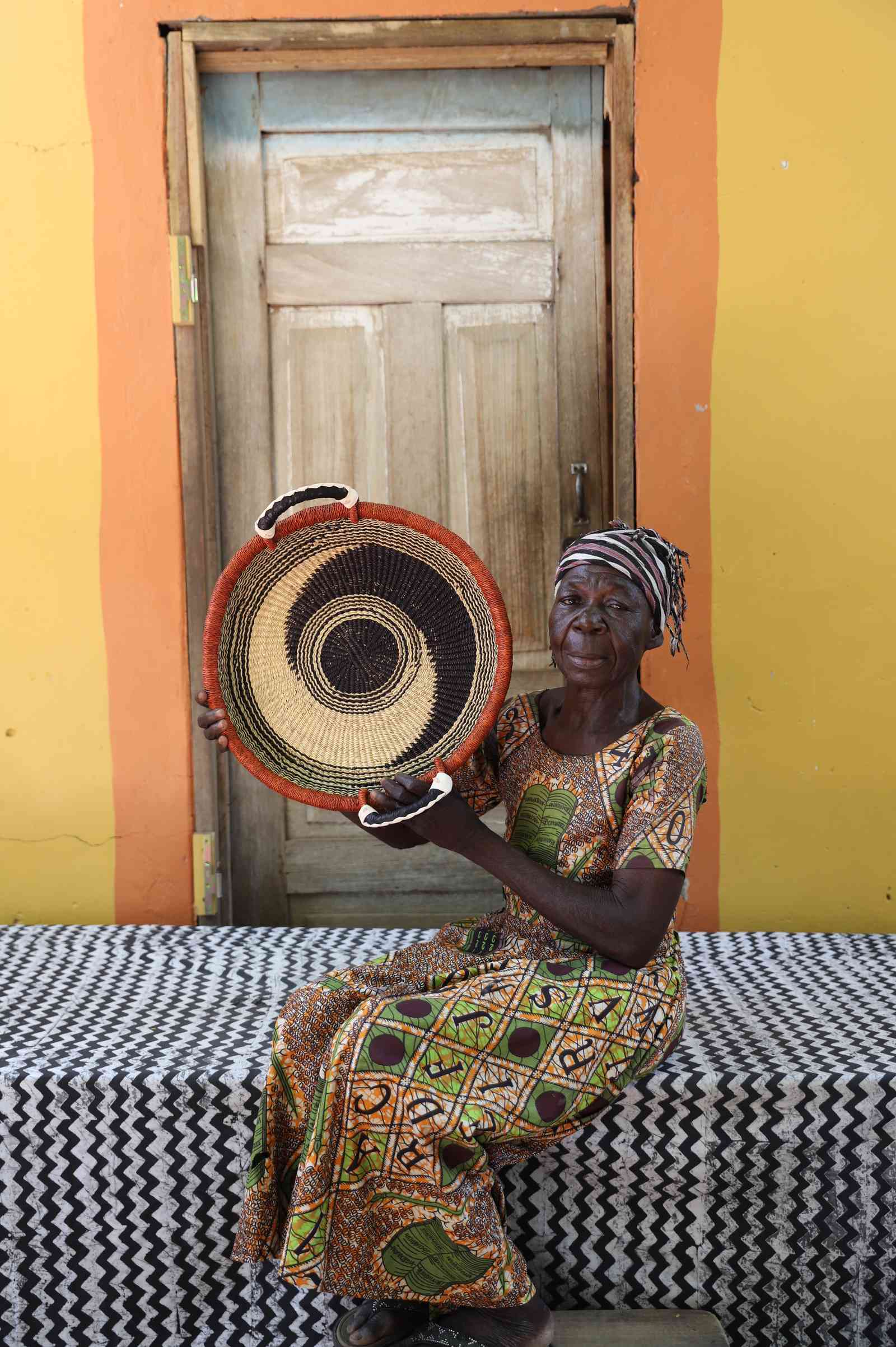 Handwoven Bolga wall tray disc with orange rim and black rings, held by a seated woman in green.