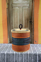 Handwoven Bolga laundry basket with coiled rim and lid in natural straw with orange bands and a dark blue centre band.