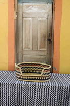 Small handwoven Bolga pet bed in natural straw with a black and orange zigzag pattern around the rim.