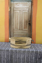 Small handwoven Bolga pet bed in natural straw with a subtle black arrow motif on the sides.