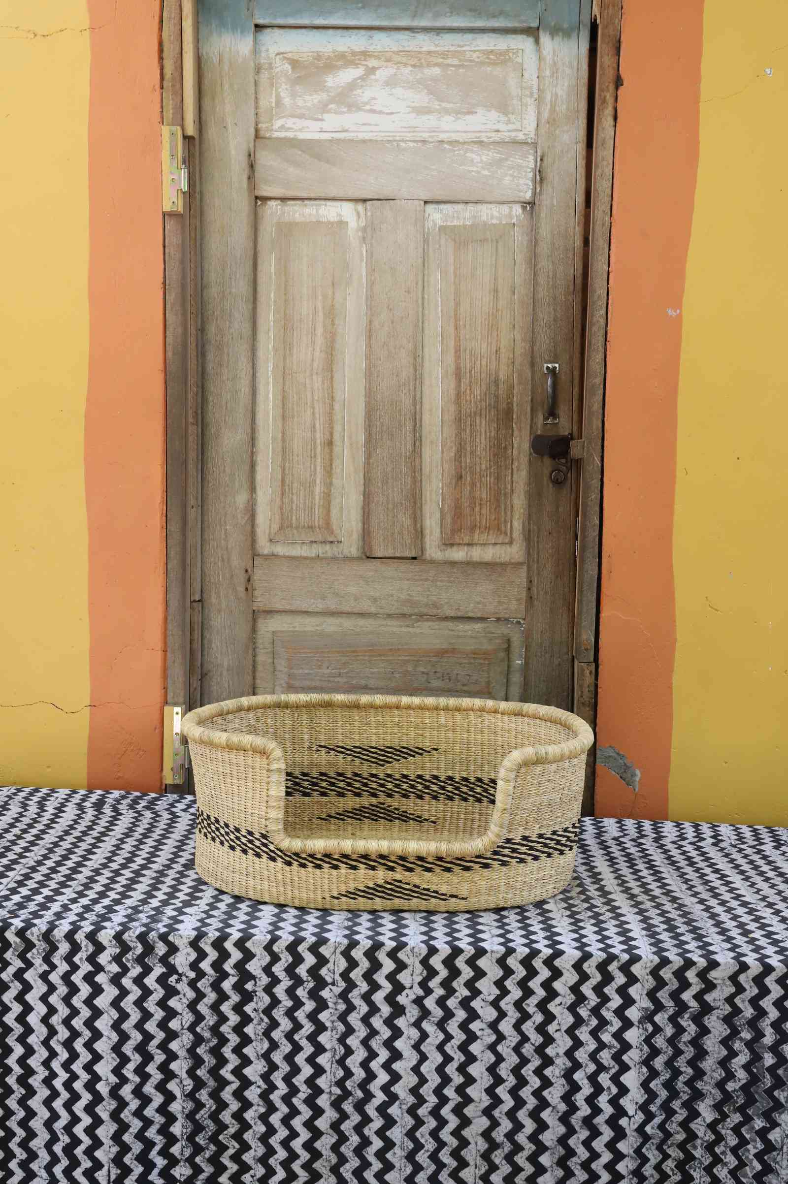 Small handwoven Bolga pet bed in natural straw with a subtle black arrow motif on the sides.