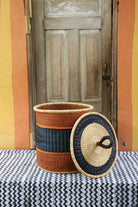 Handwoven Bolga laundry basket with lid removed, natural body with orange and dark blue bands and matching lid.