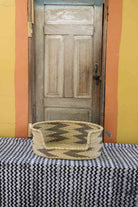 Small handwoven Bolga pet bed in natural straw with a bold black arrow and triangle pattern.