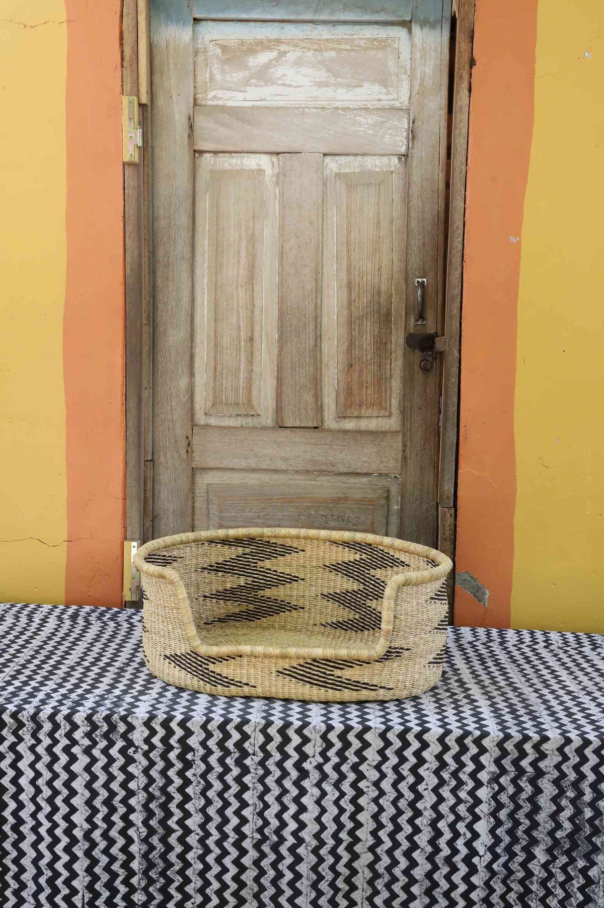 Small handwoven Bolga pet bed in natural straw with a bold black arrow and triangle pattern.