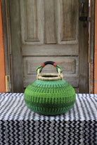 Large handwoven Bolga pot basket in lime green elephant grass with a leather top handle, on a chevron surface.