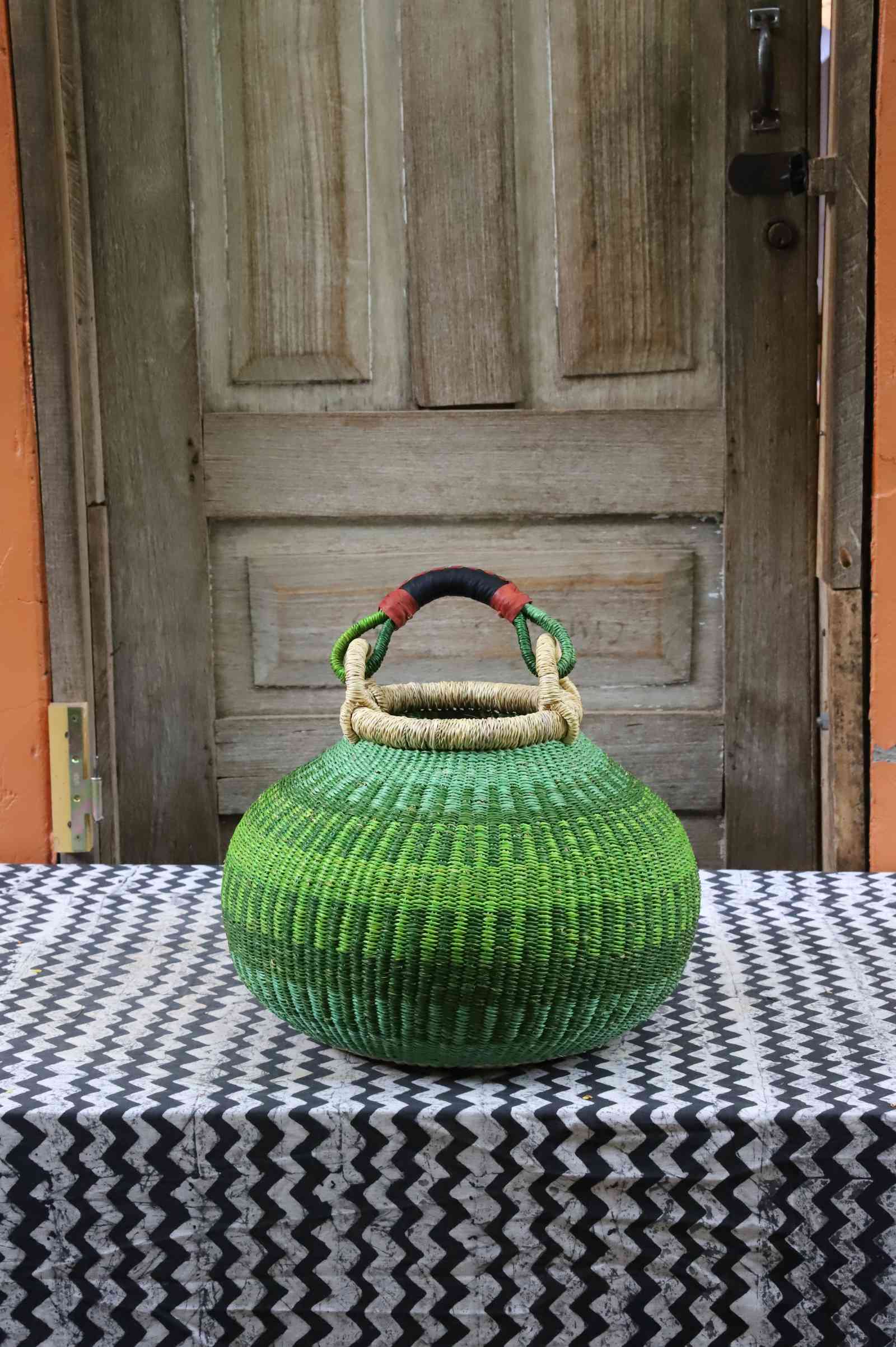 Large handwoven Bolga pot basket in lime green elephant grass with a leather top handle, on a chevron surface.