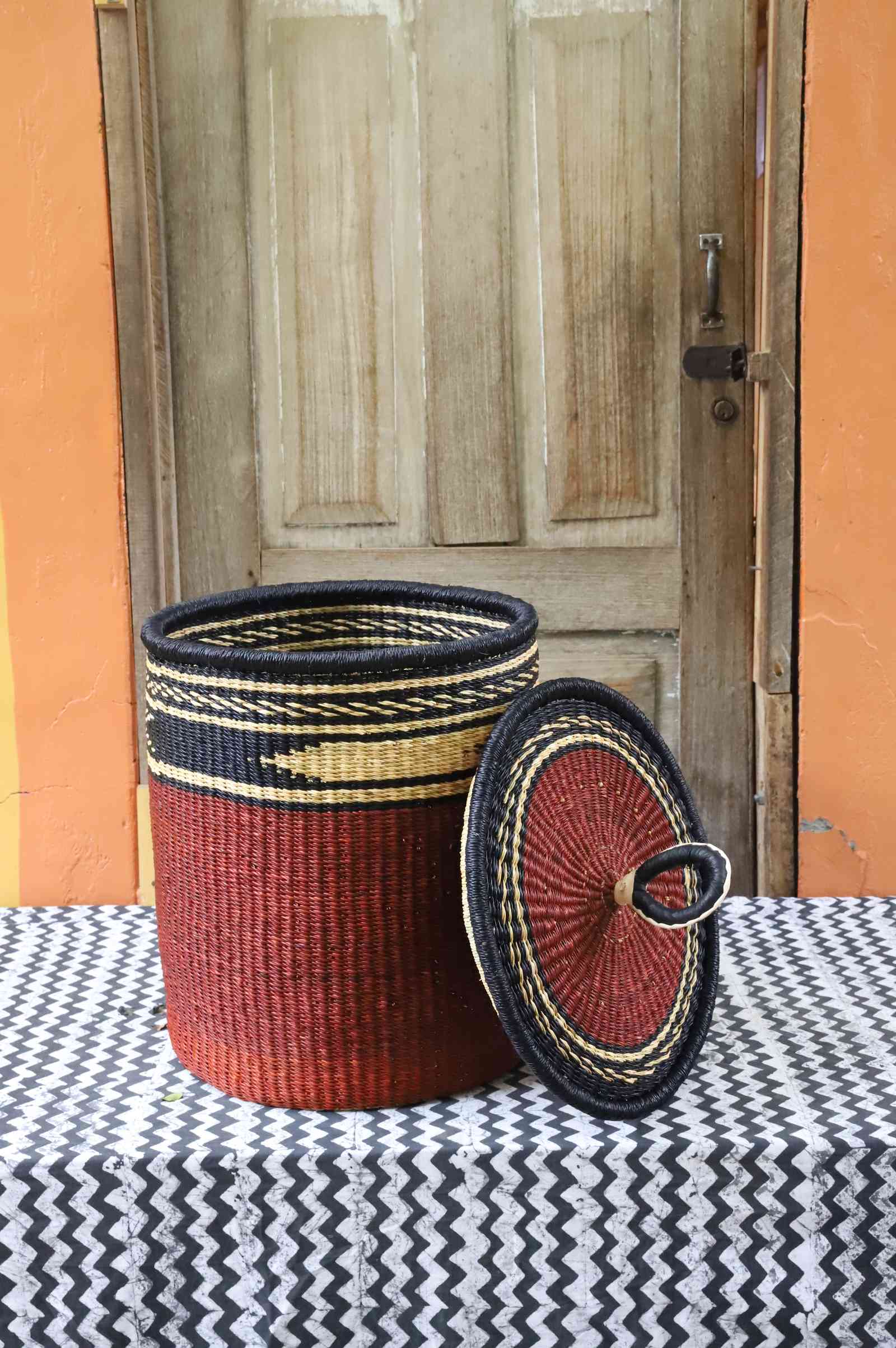 Coiled-rim laundry basket in solid rust weave, lid resting alongside on a chevron cloth.
