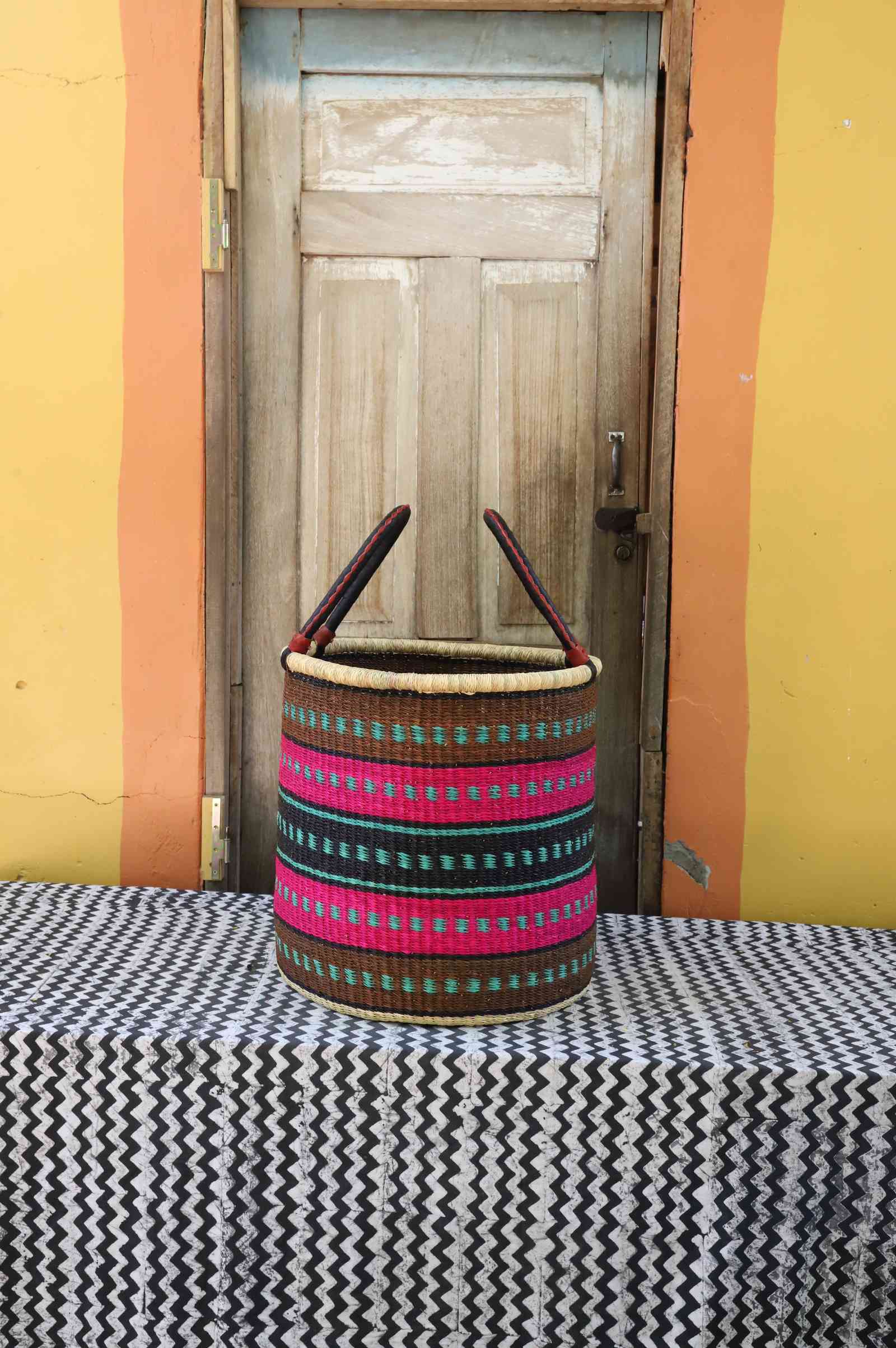 Large handwoven open-top Bolga laundry basket in natural straw with pink and dark banded stripes.