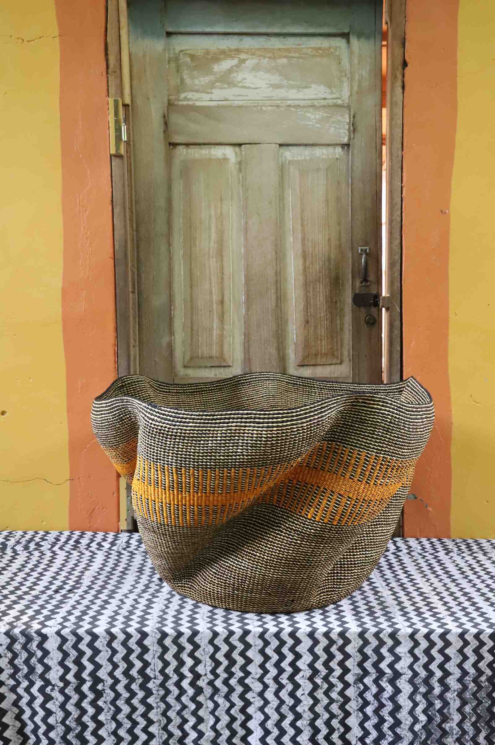 Large sculptural Bolga basket with a wavy rim, woven in grey and natural tones with an orange stripe, on a tablecloth.