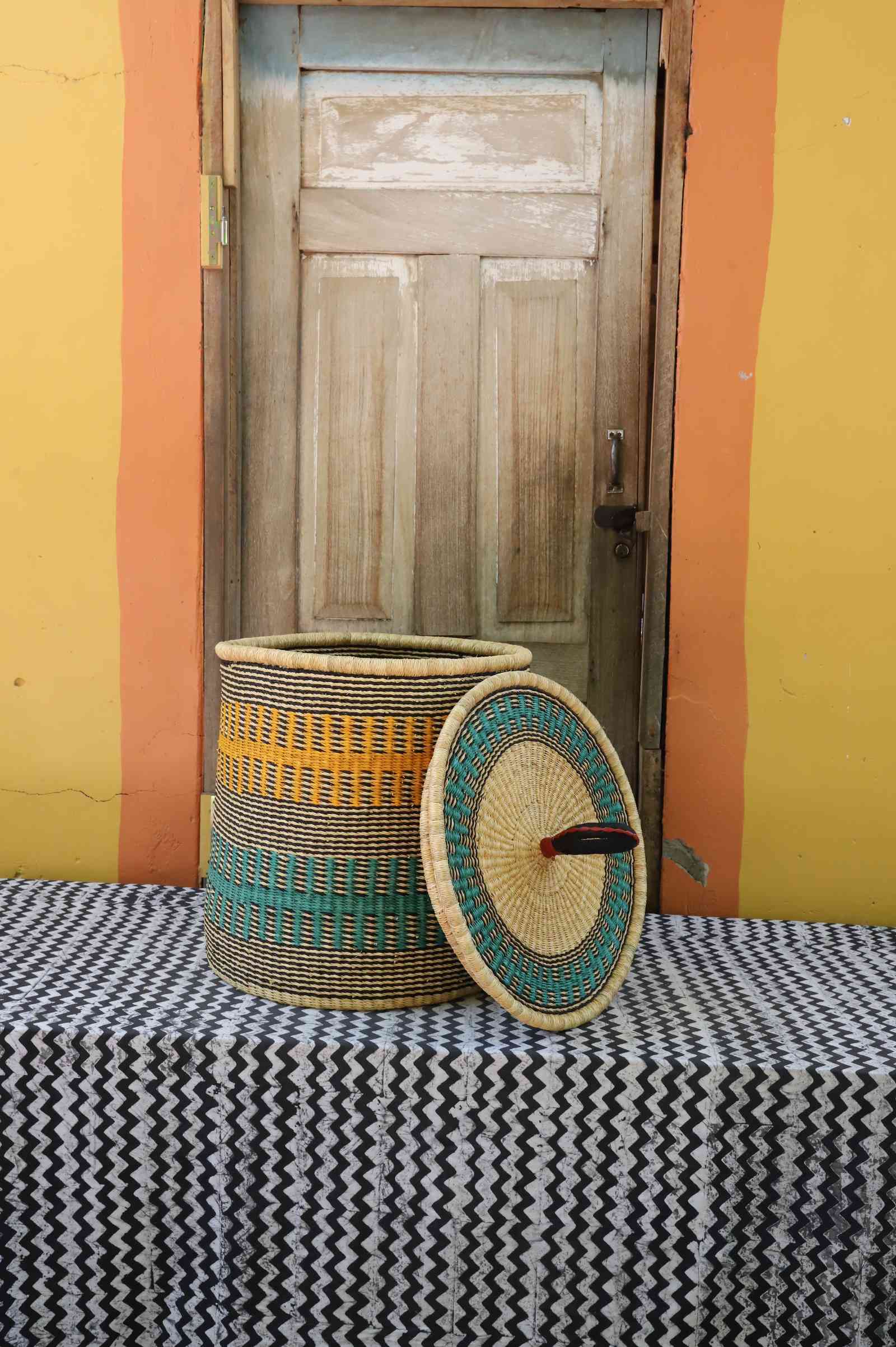 Handwoven Bolga laundry basket with lid removed, natural body with yellow and teal bands and matching lid.