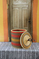 Handwoven Bolga laundry basket with lid removed, natural body with red, orange and yellow bands and matching lid.
