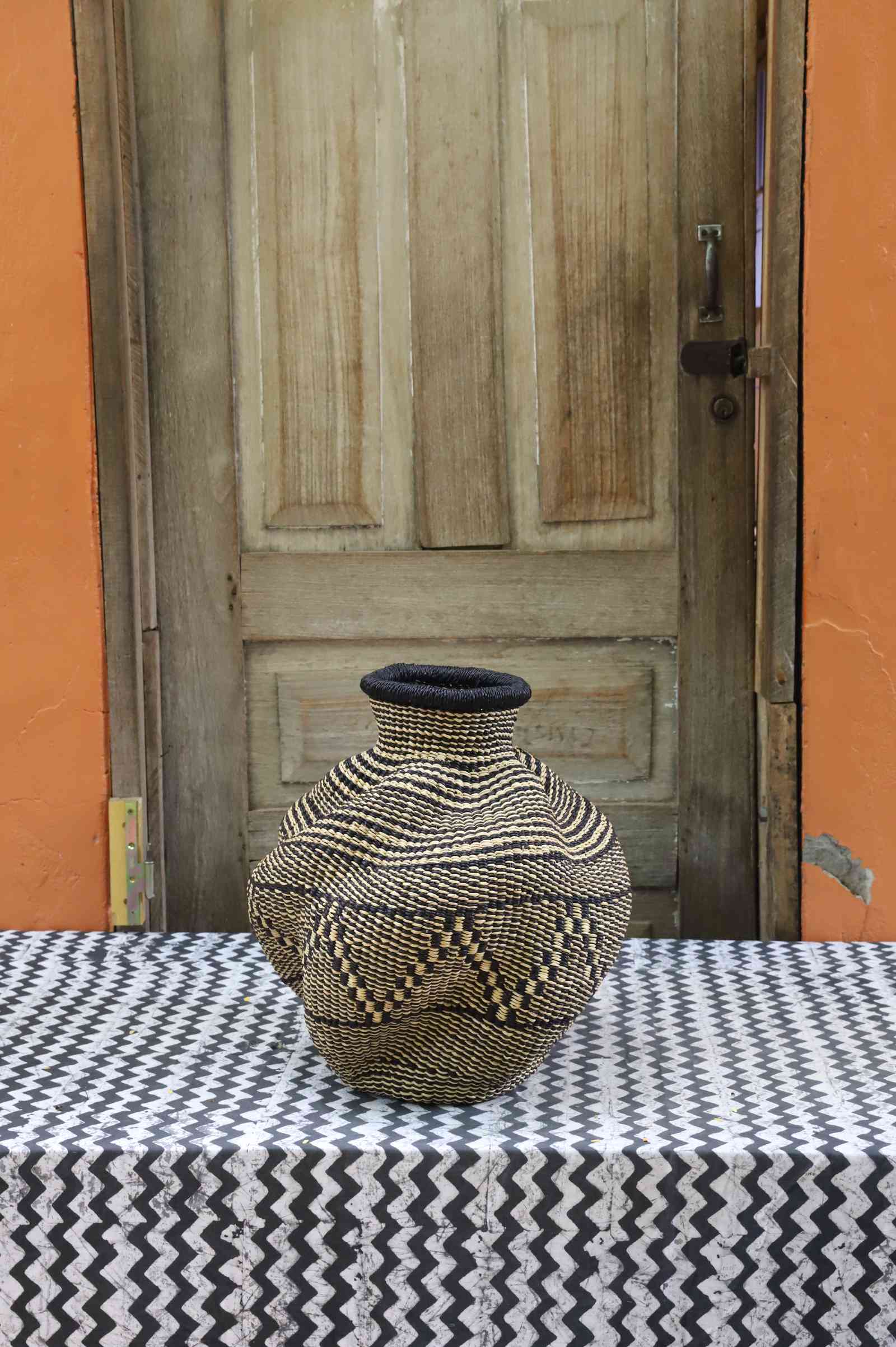 Handwoven Bolga art basket in an urn shape, natural straw with a fine dark diamond weave and dark rim.
