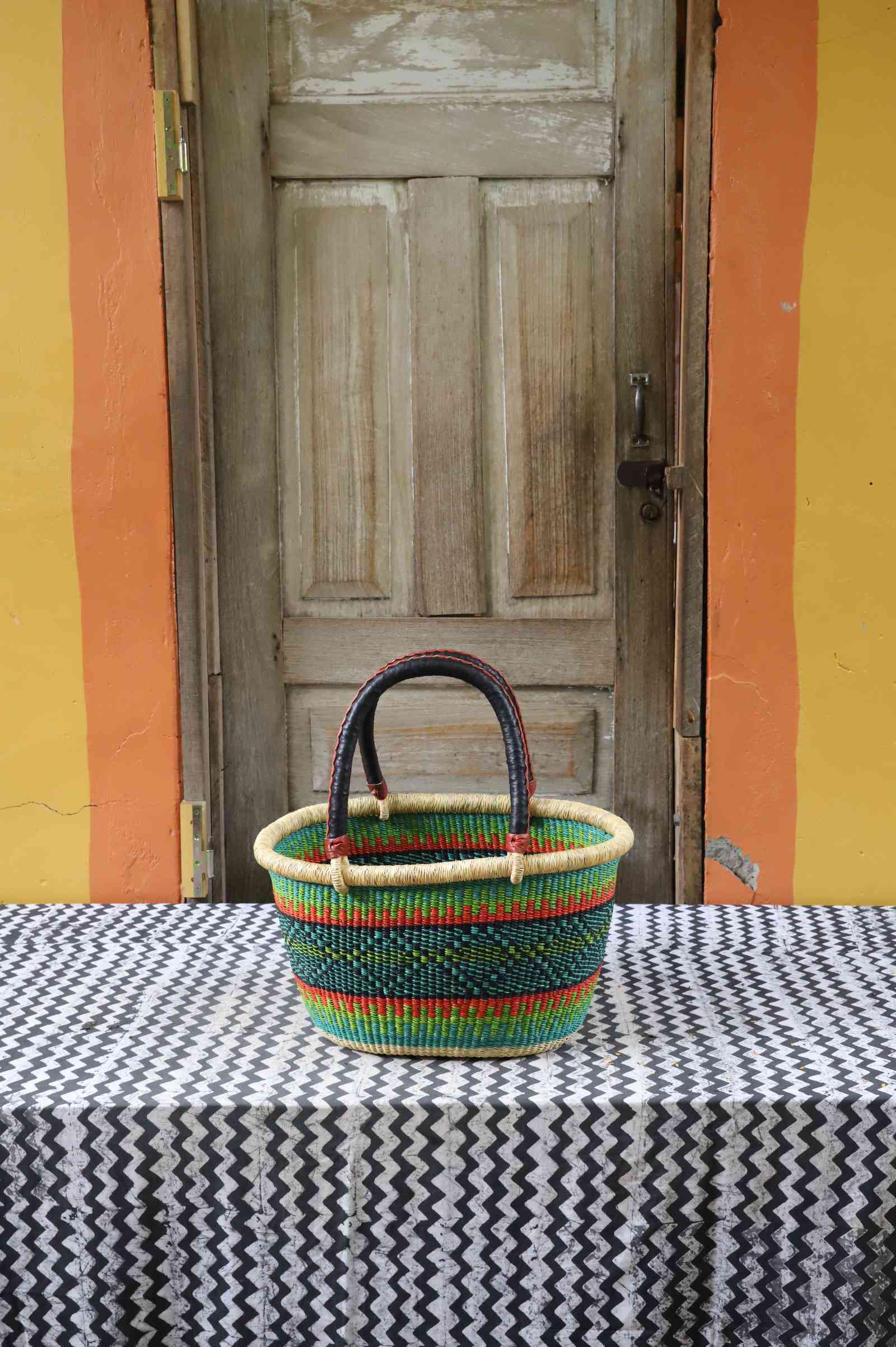 Medium handwoven oval Bolga shopping basket in dyed green with red and yellow banded accent stripes.