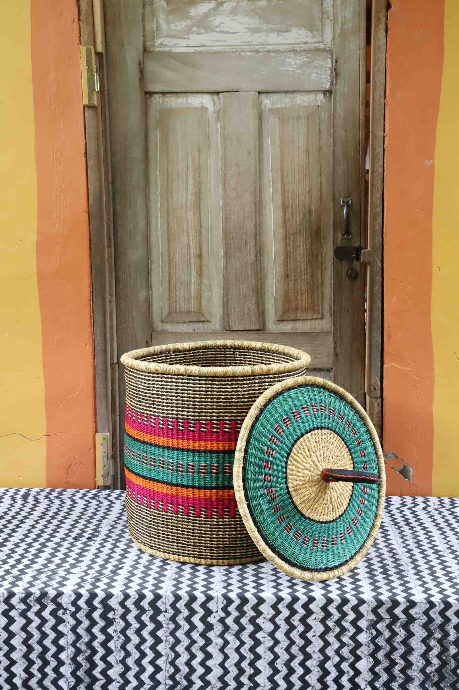Handwoven Bolga laundry basket with lid removed, natural body with pink, orange, green and teal stripes.