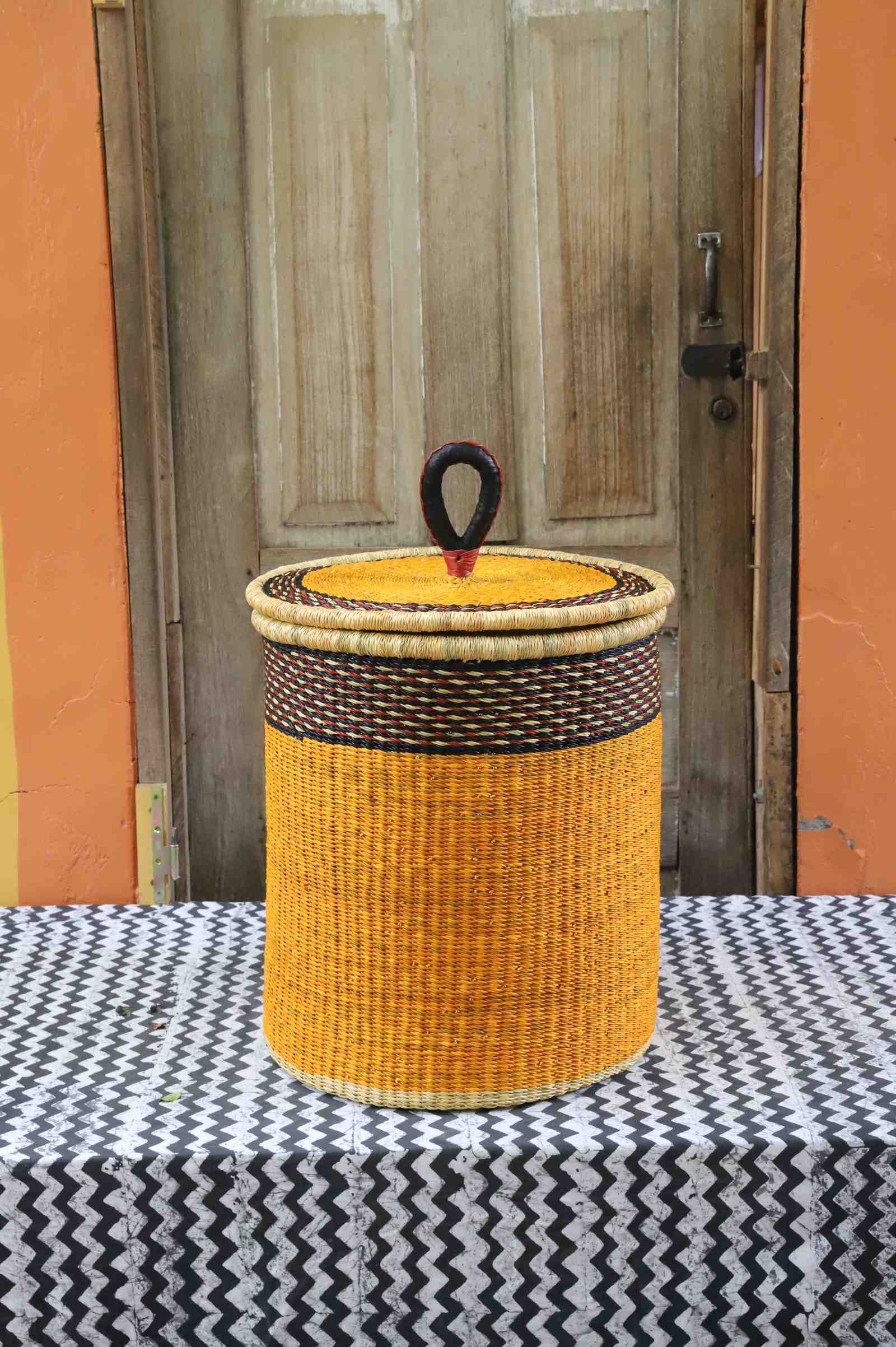 Coiled-rim lidded laundry basket in solid mustard weave with a black rim band, styled on a chevron cloth.