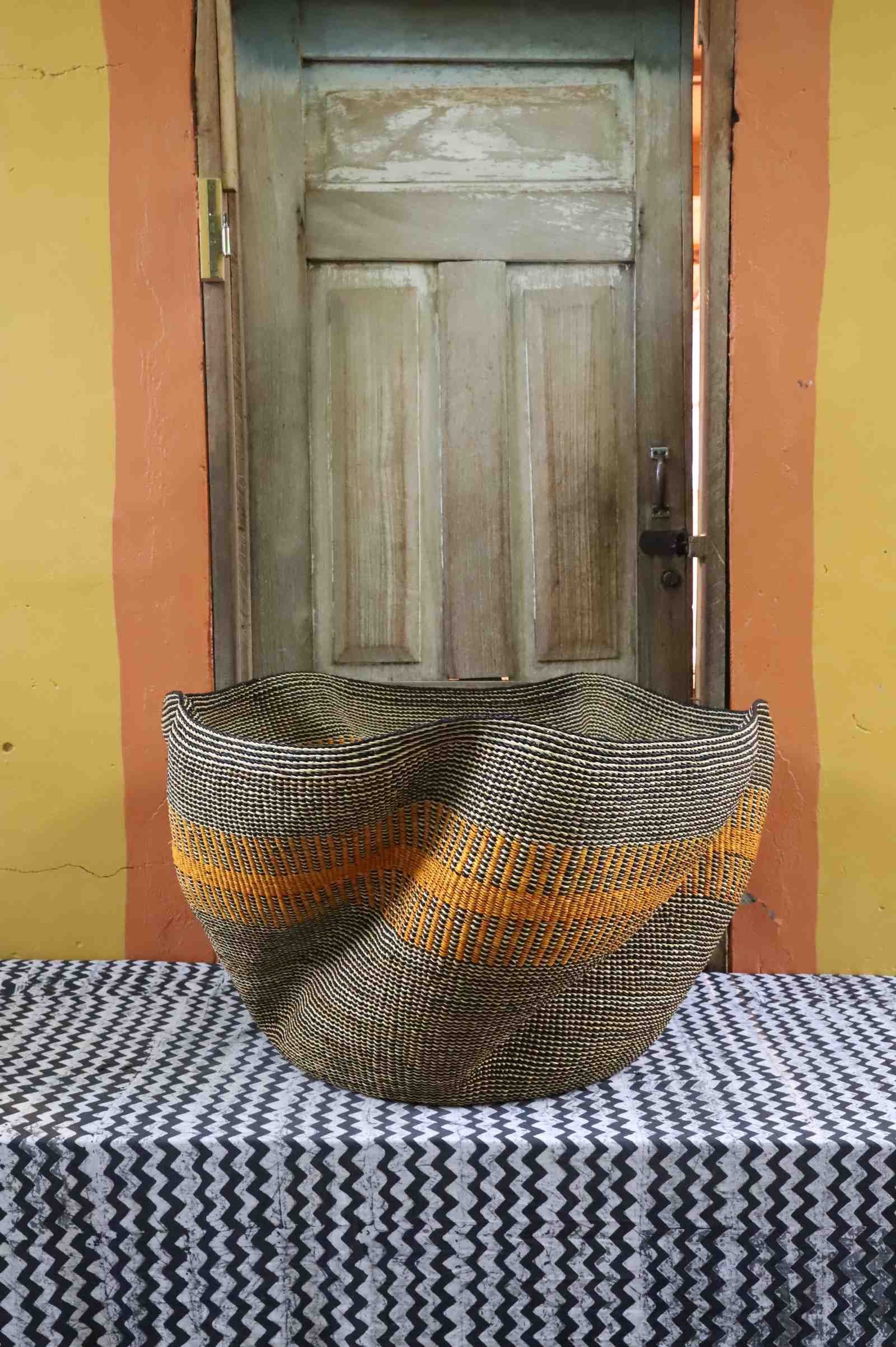 Sculptural Bolga basket with an undulating wavy rim, woven in grey and natural tones with an orange stripe band.