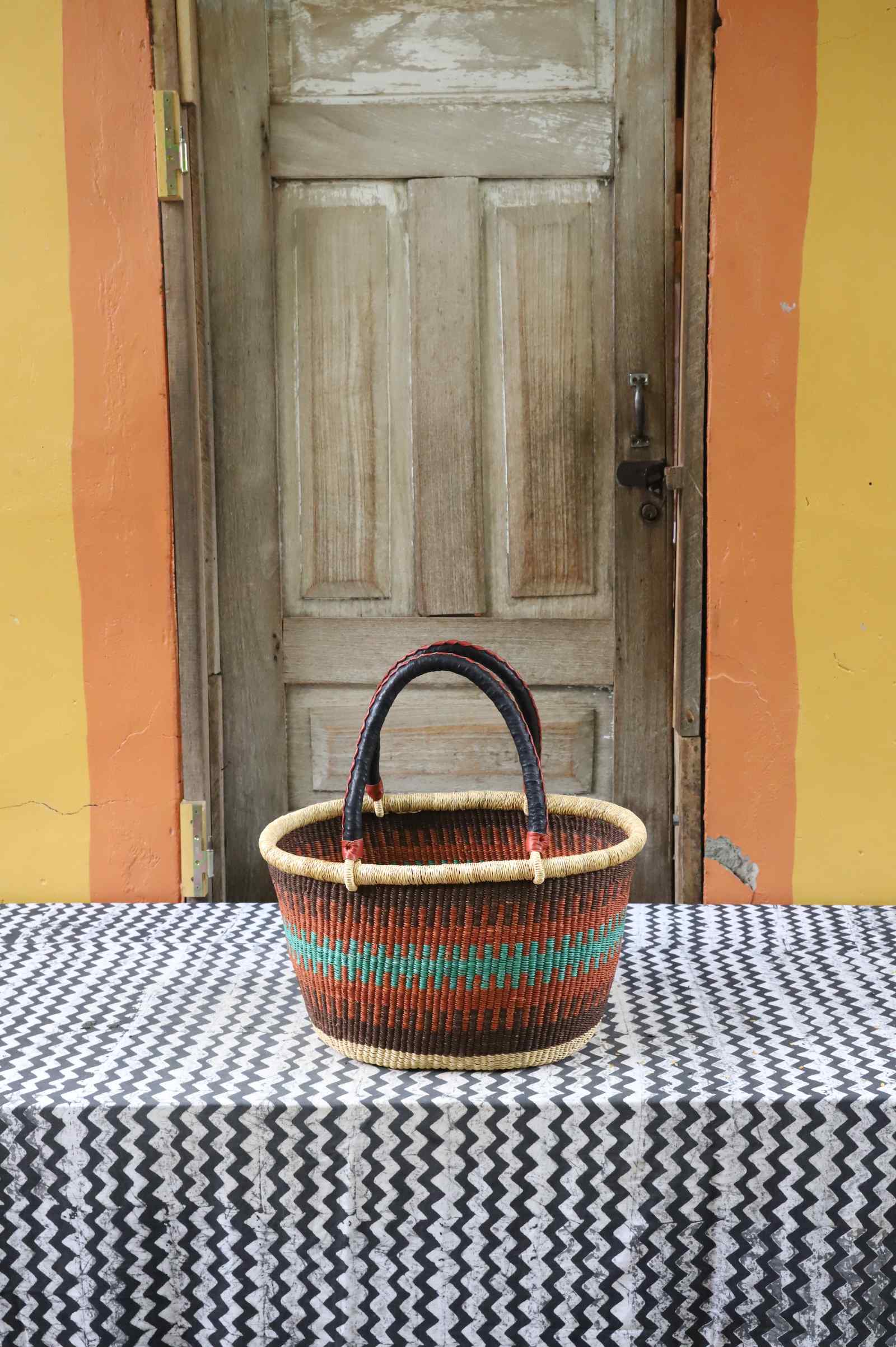 Medium handwoven oval Bolga shopping basket in natural straw with orange and teal banded stripes.