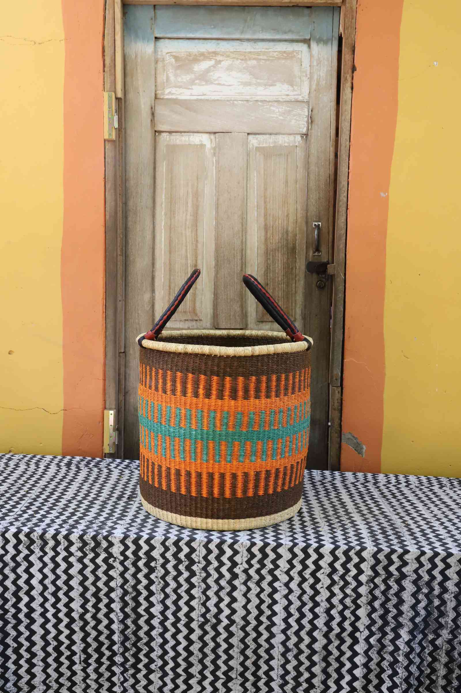 Large handwoven open-top Bolga laundry basket in brown, orange and teal banded stripes.