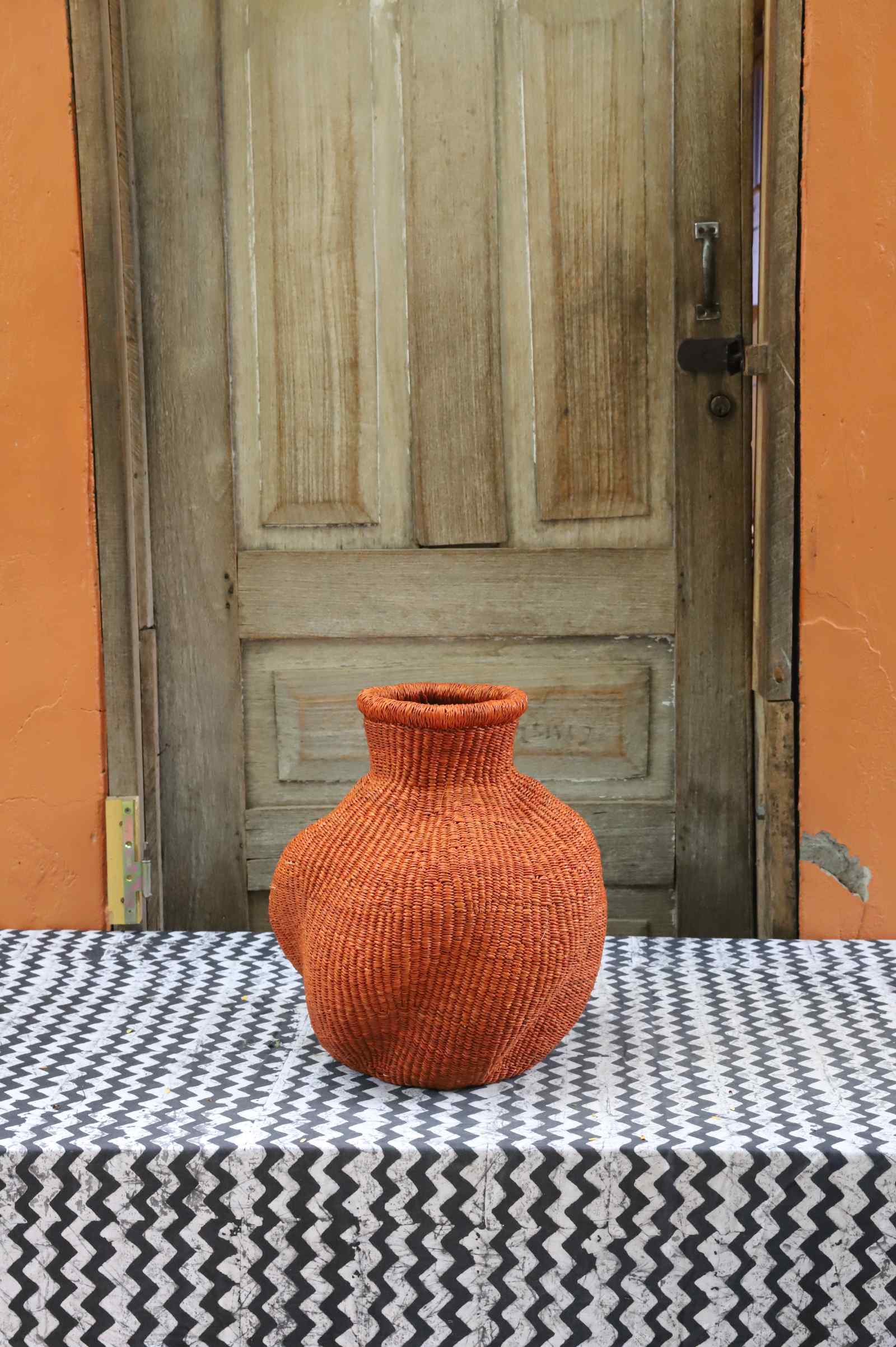 Handwoven Bolga art basket in an urn shape, dyed rust-orange with a dark rim collar.