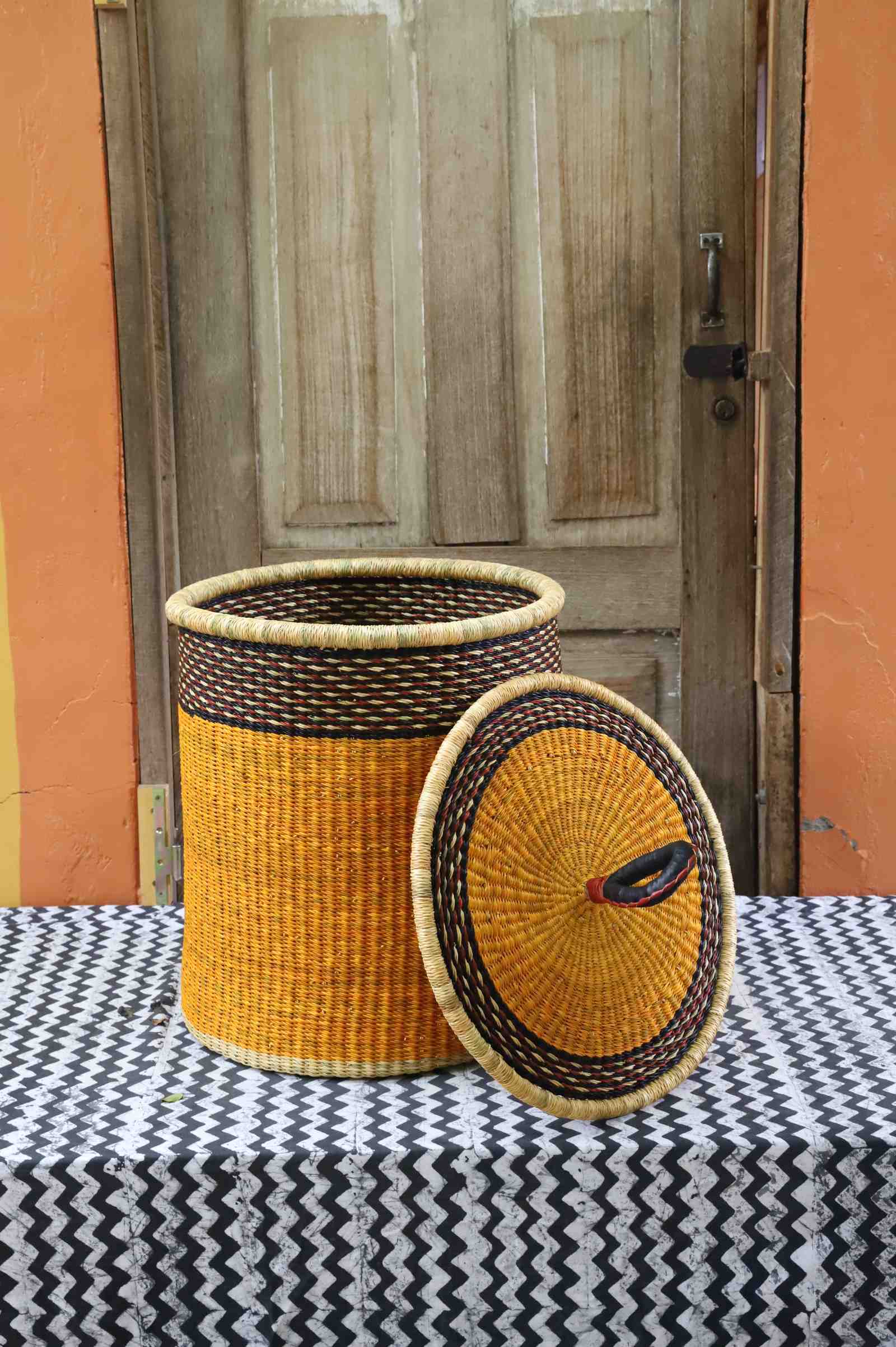 Coiled-rim laundry basket in solid mustard weave, lid resting alongside on a chevron cloth.