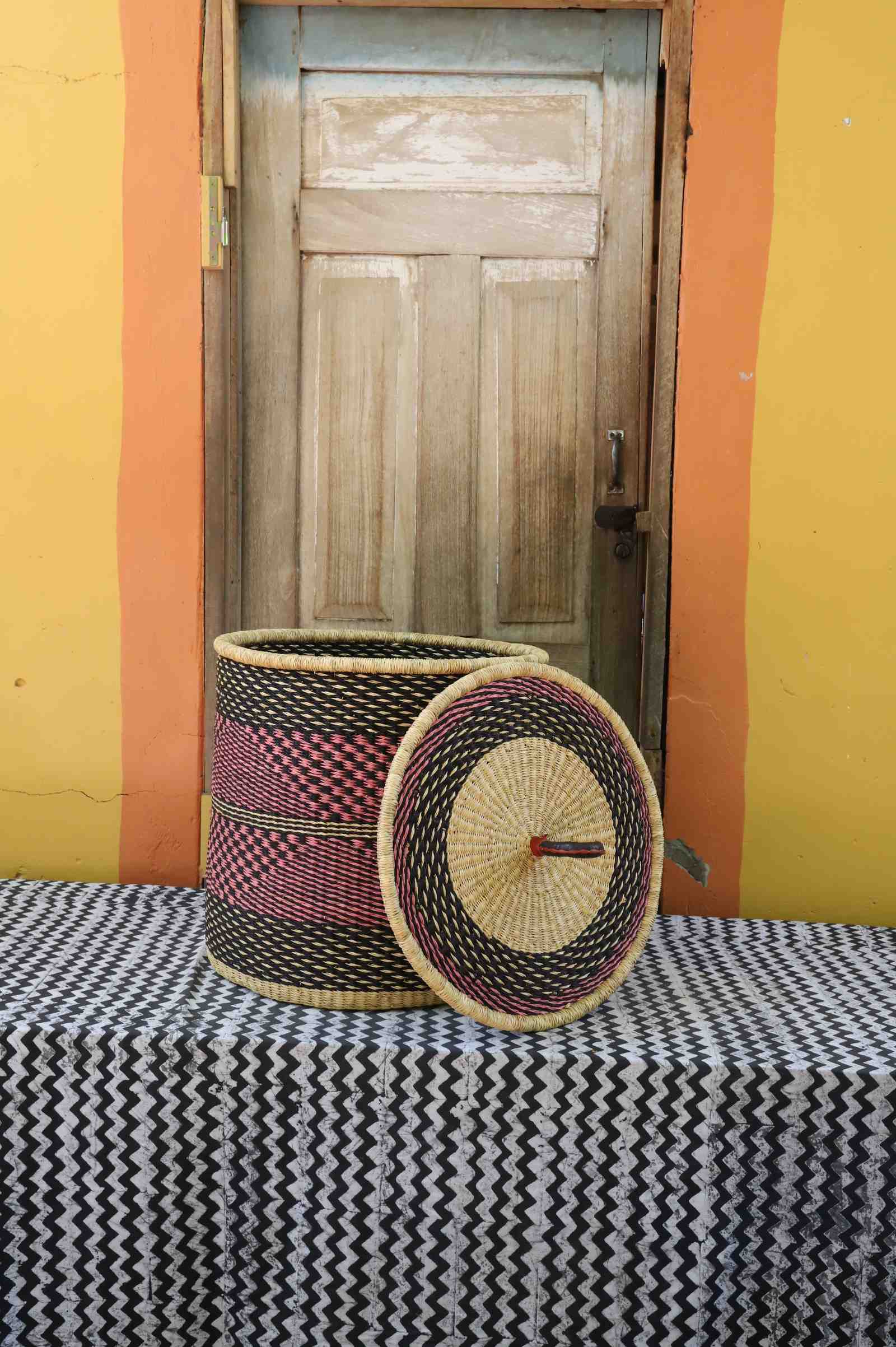 Handwoven Bolga laundry basket with lid removed, natural body with red checkered band and matching lid.