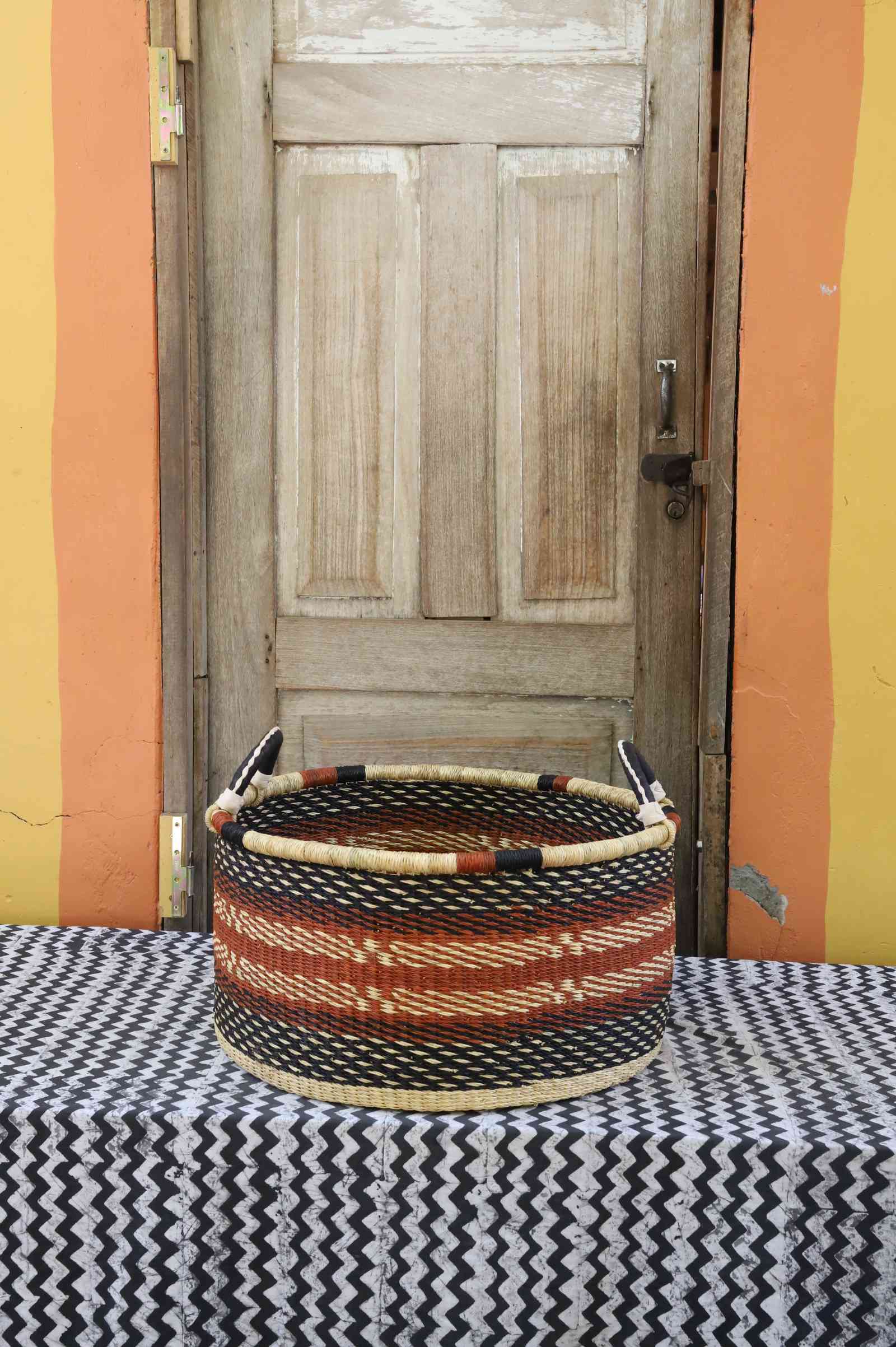 Large handwoven Bolga storage tub in natural straw with orange and black diamond weave patterns.