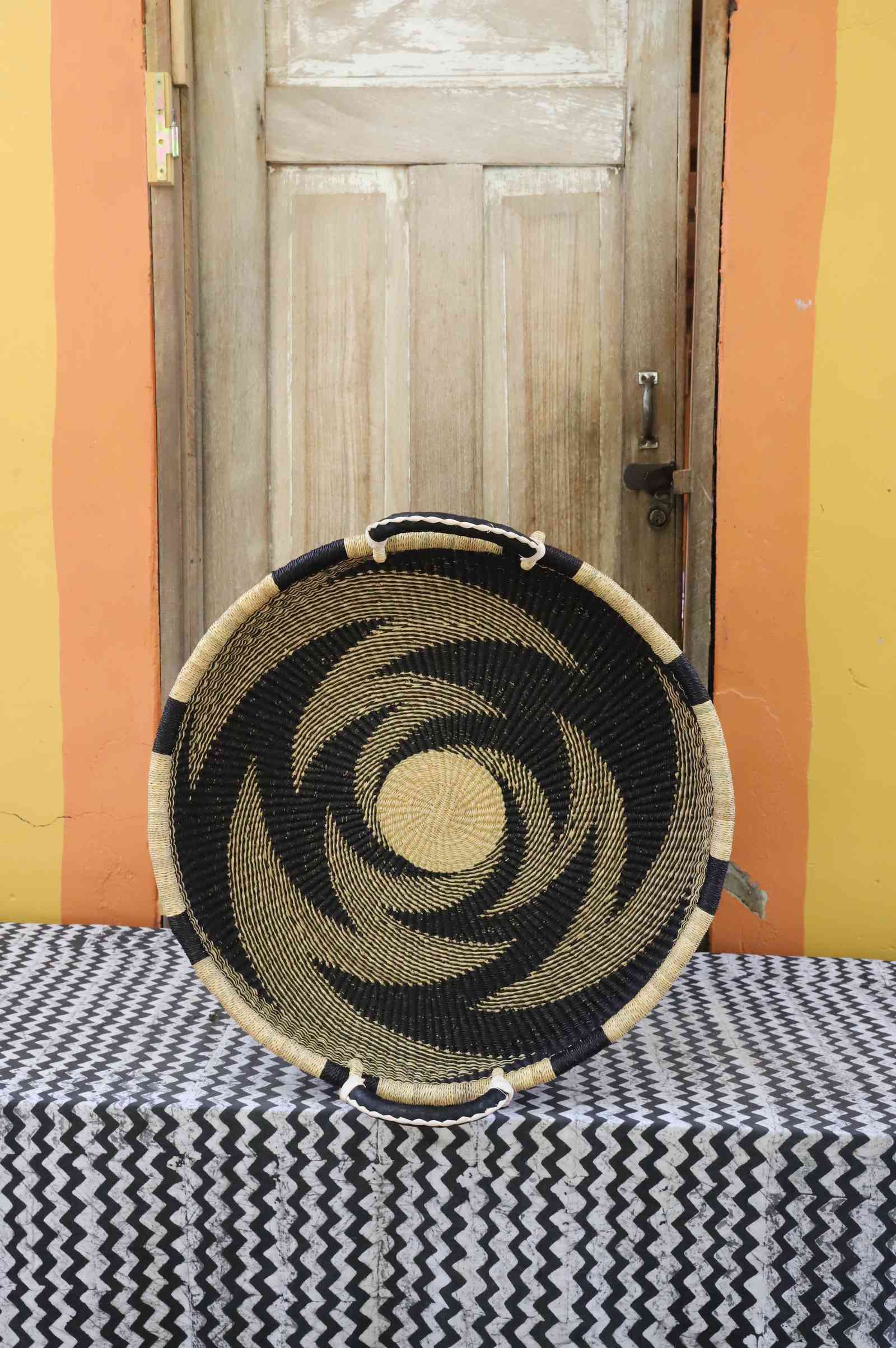 Medium handwoven Bolga wall tray disc in natural straw with a bold black pinwheel swirl.