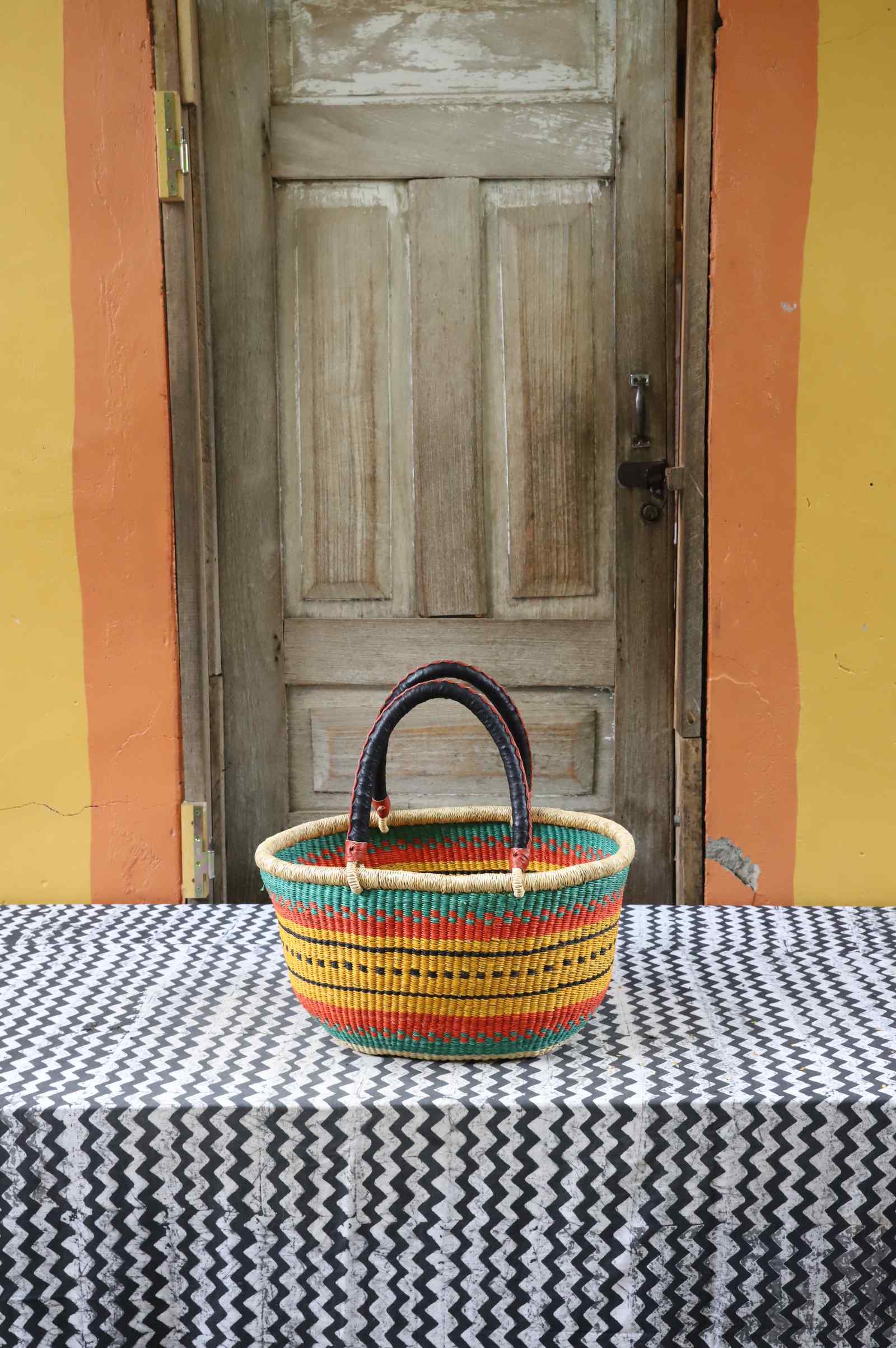 Medium handwoven oval Bolga shopping basket in natural straw with orange, green and red banded stripes.