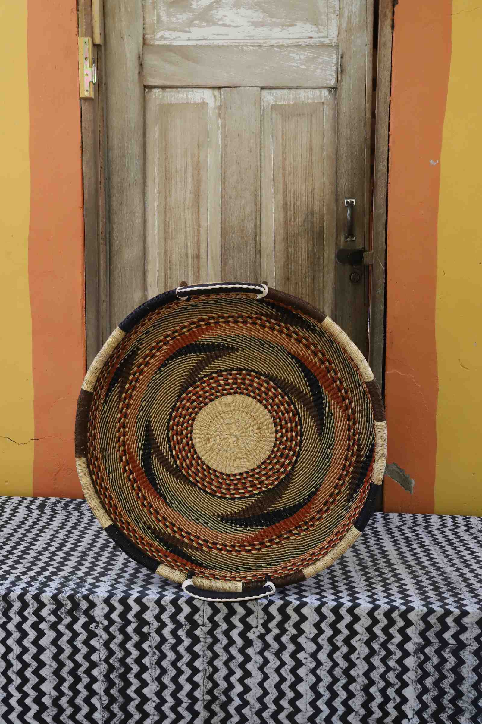 Medium handwoven Bolga wall tray disc with fine brown, black and orange concentric bands and yellow centre.