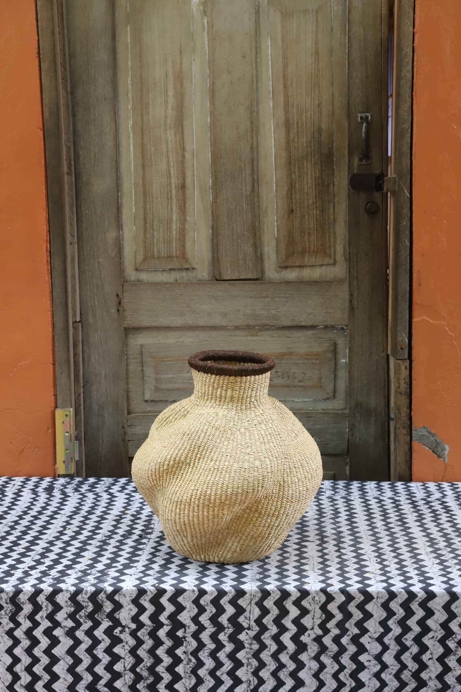 Handwoven Bolga art basket in an urn shape, all natural straw with a dark rim collar.
