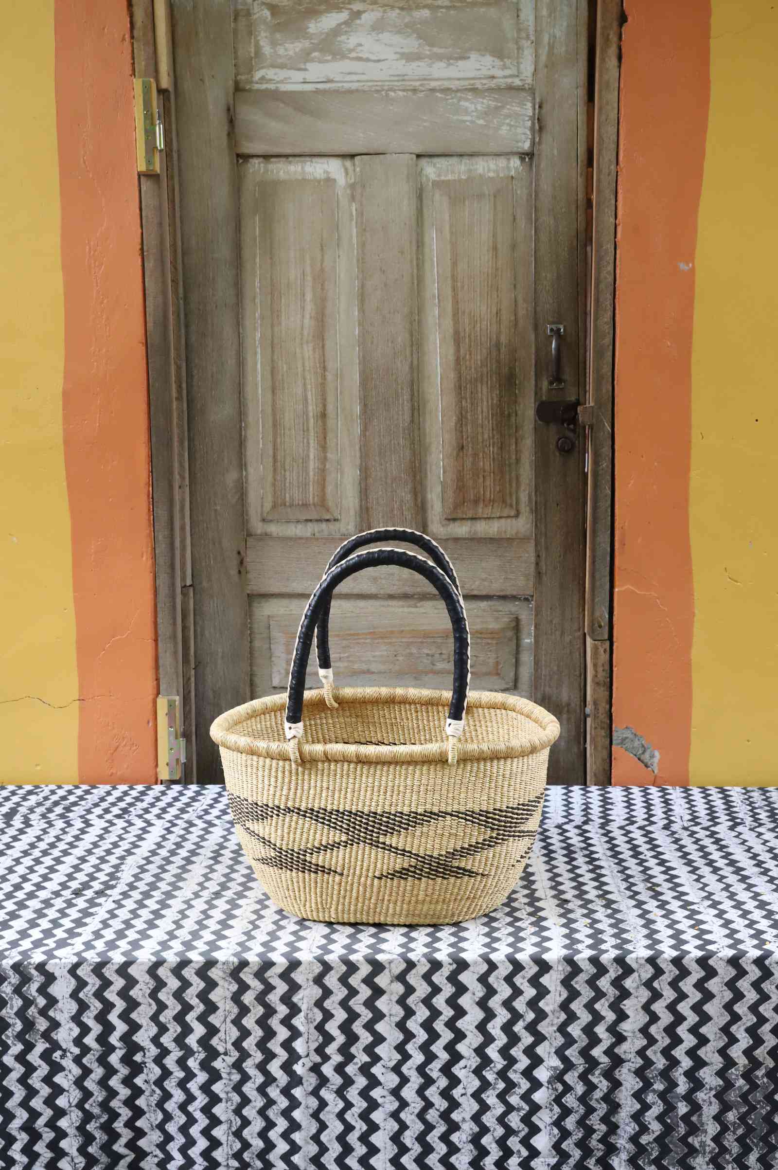 Medium handwoven oval Bolga shopping basket in natural straw with dark banded stripes and dark handles.