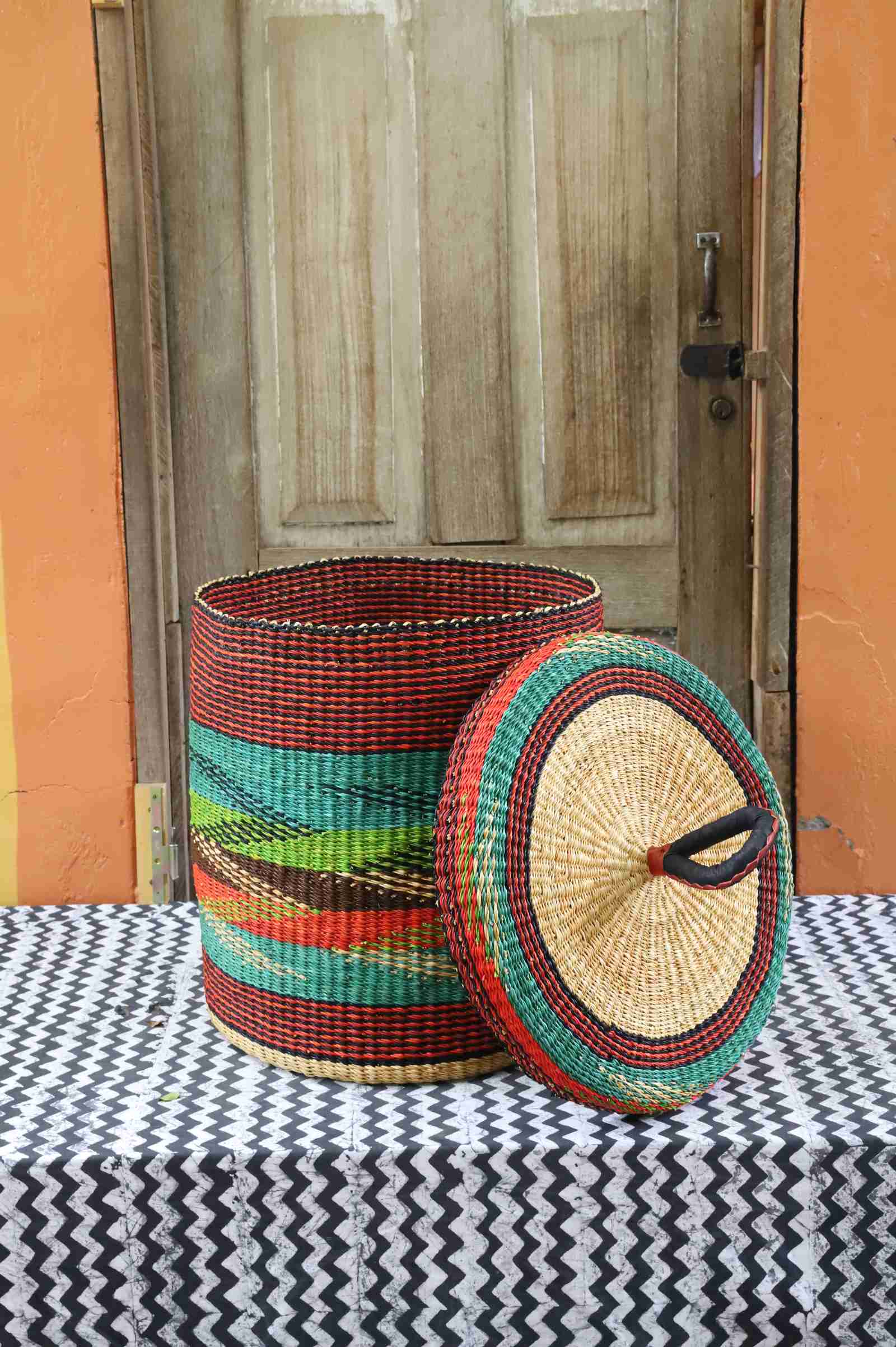 Lidded laundry basket in rust and teal wave-patterned weave, lid resting alongside on a chevron cloth.