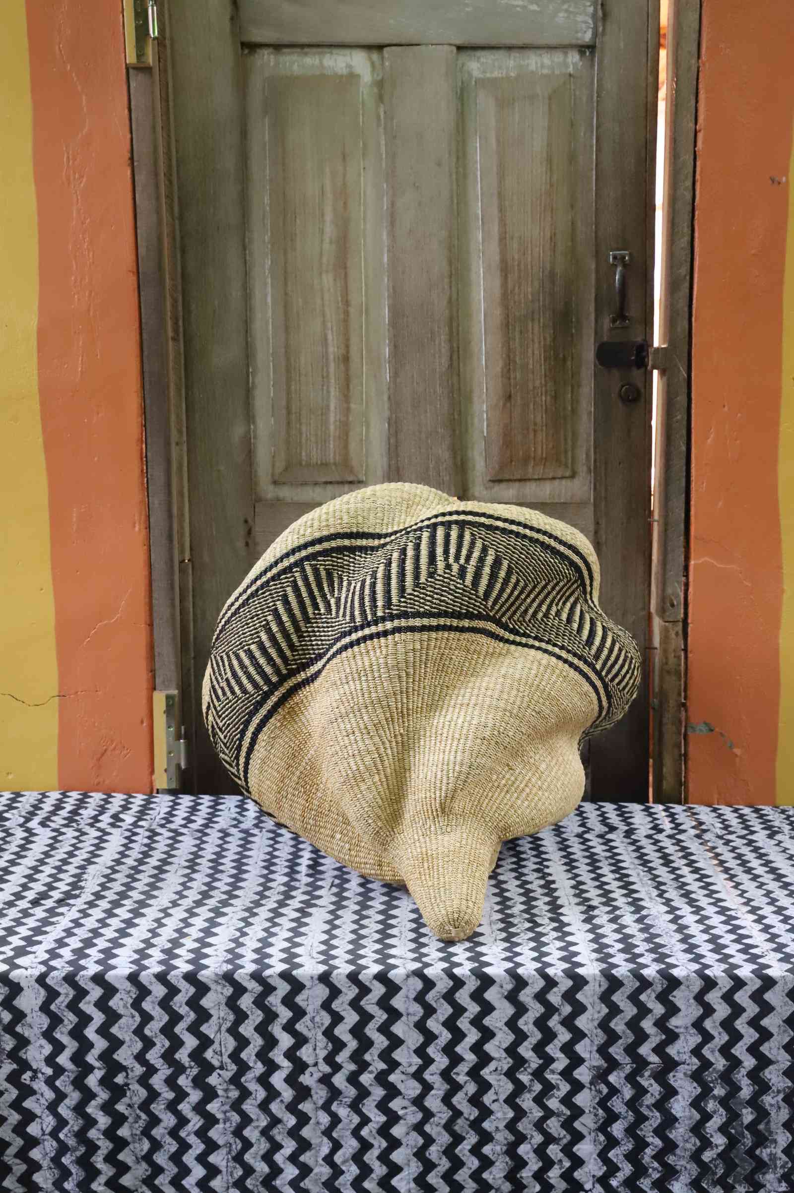 Spiral-form Bolga basket in natural straw with a bold black geometric band, angled to show its curved silhouette.