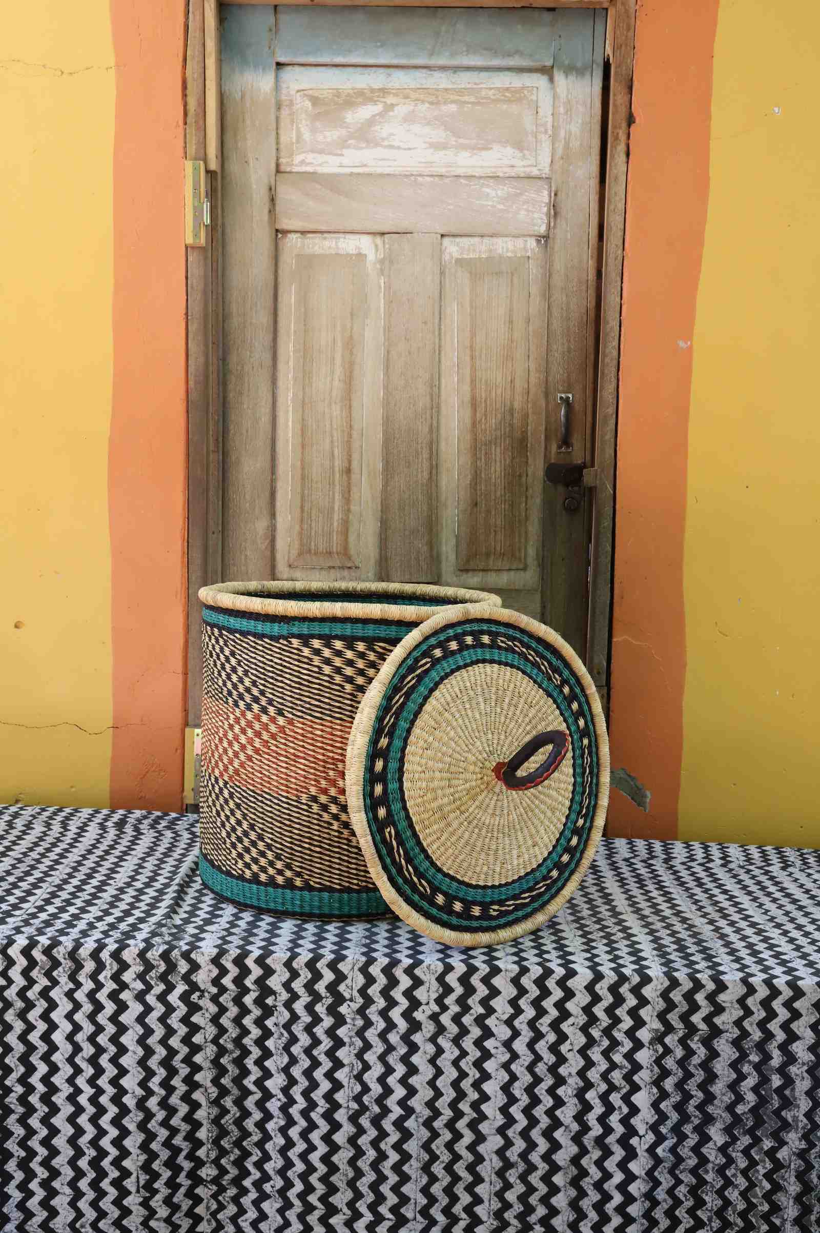 Handwoven Bolga laundry basket with lid removed, natural body with orange bands and teal rim accent.