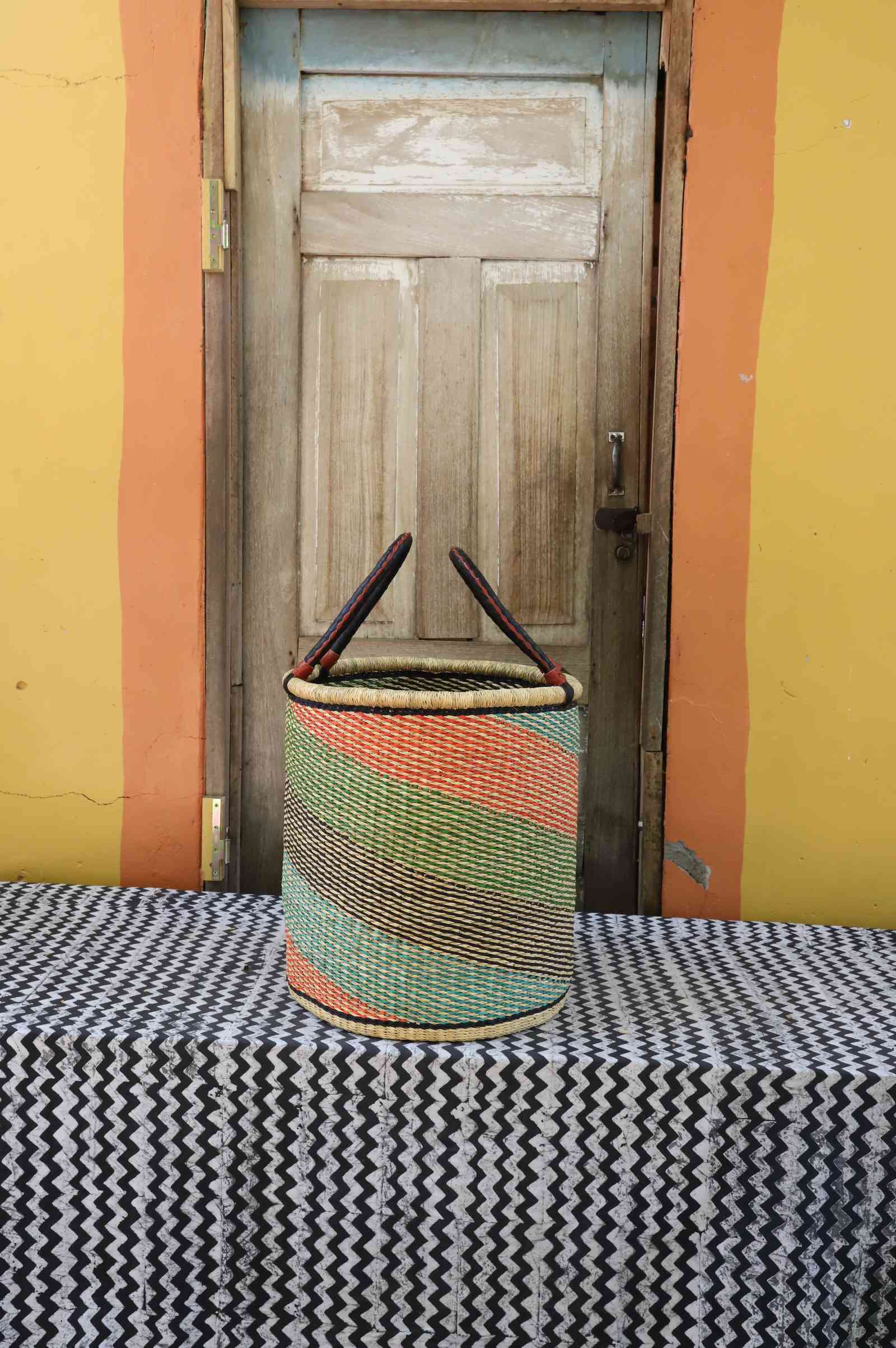Medium handwoven open-top Bolga laundry basket in natural straw with green, orange and pink diagonal stripes.