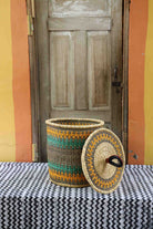 Handwoven Bolga laundry basket with lid removed, natural body with orange and teal bands and matching lid.